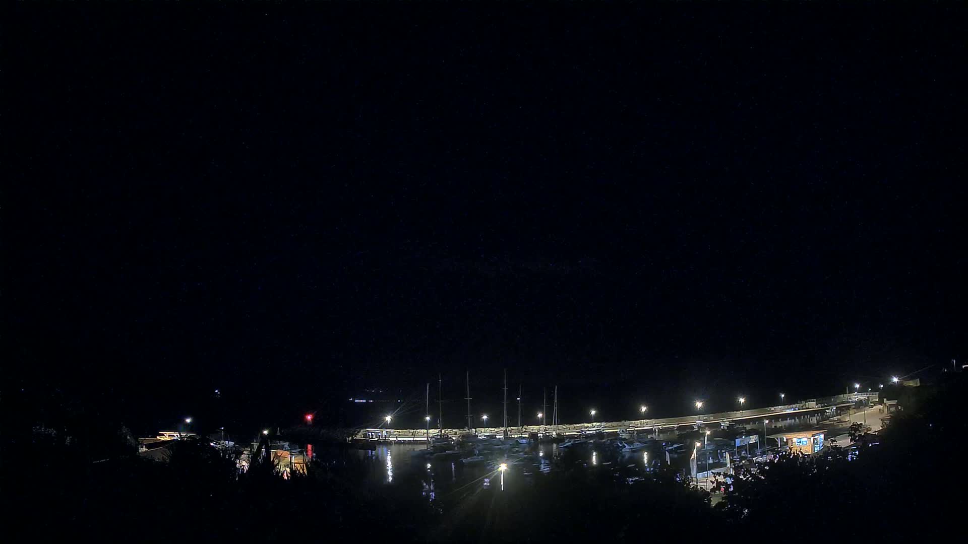 A nighttime view of a marina with boats docked, illuminated by lights under a clear, dark sky.