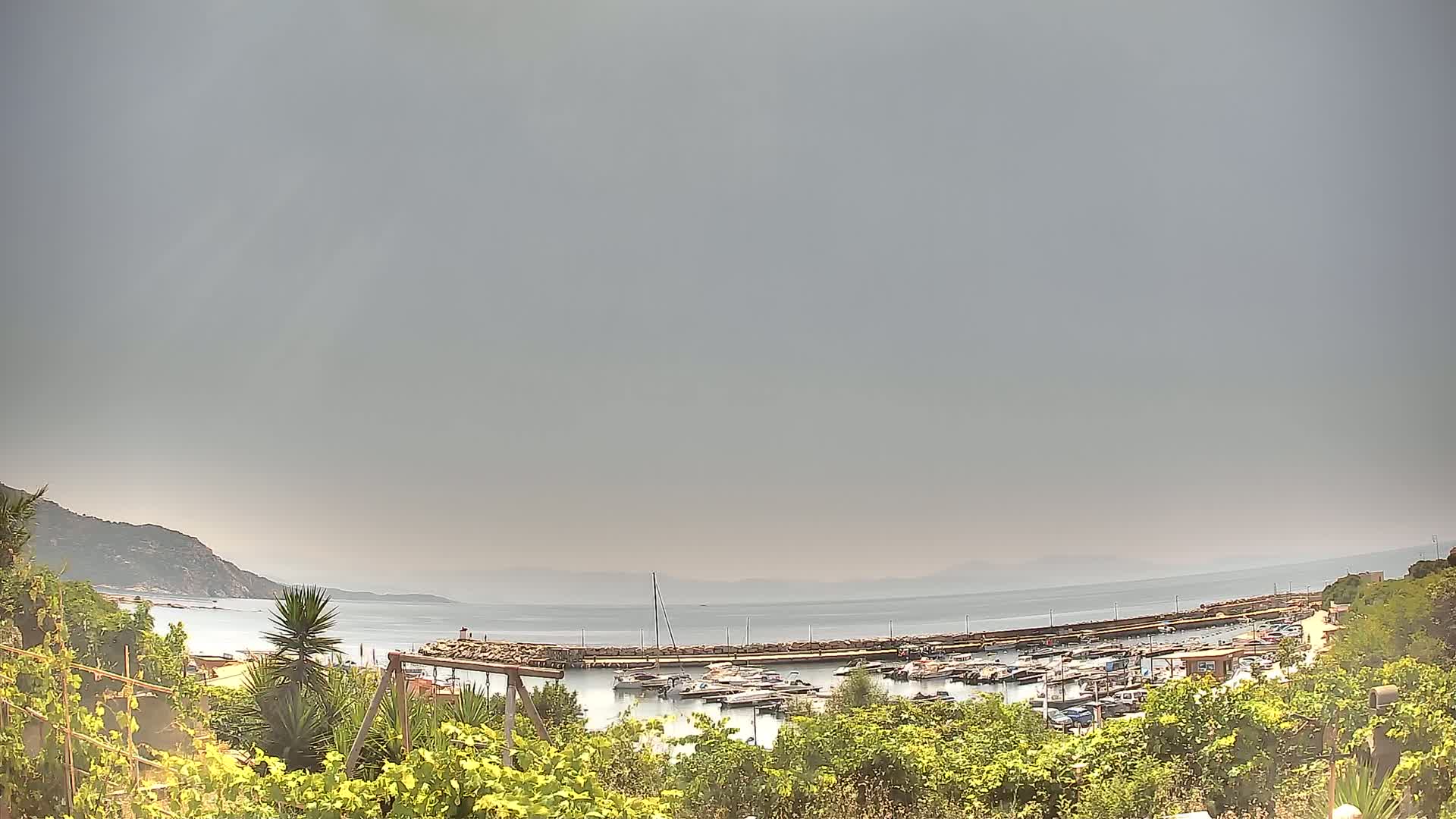A hazy, overcast day reveals a small harbor filled with boats nestled between a rocky coastline and calm sea.