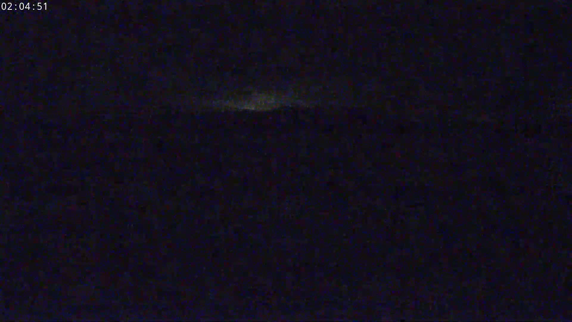 A dark, nighttime scene shows a faintly illuminated horizon under a mostly clear sky.