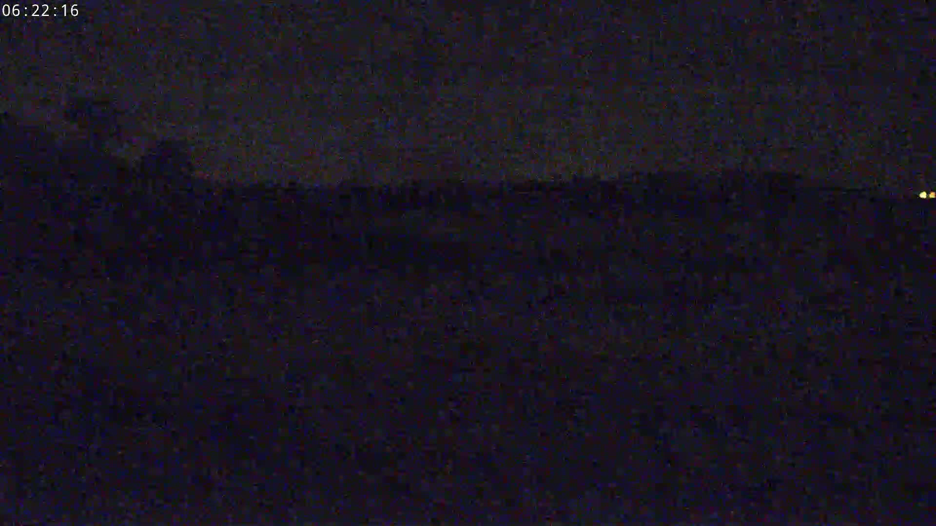 A dark, nighttime landscape is visible, with a few faint lights in the distance.