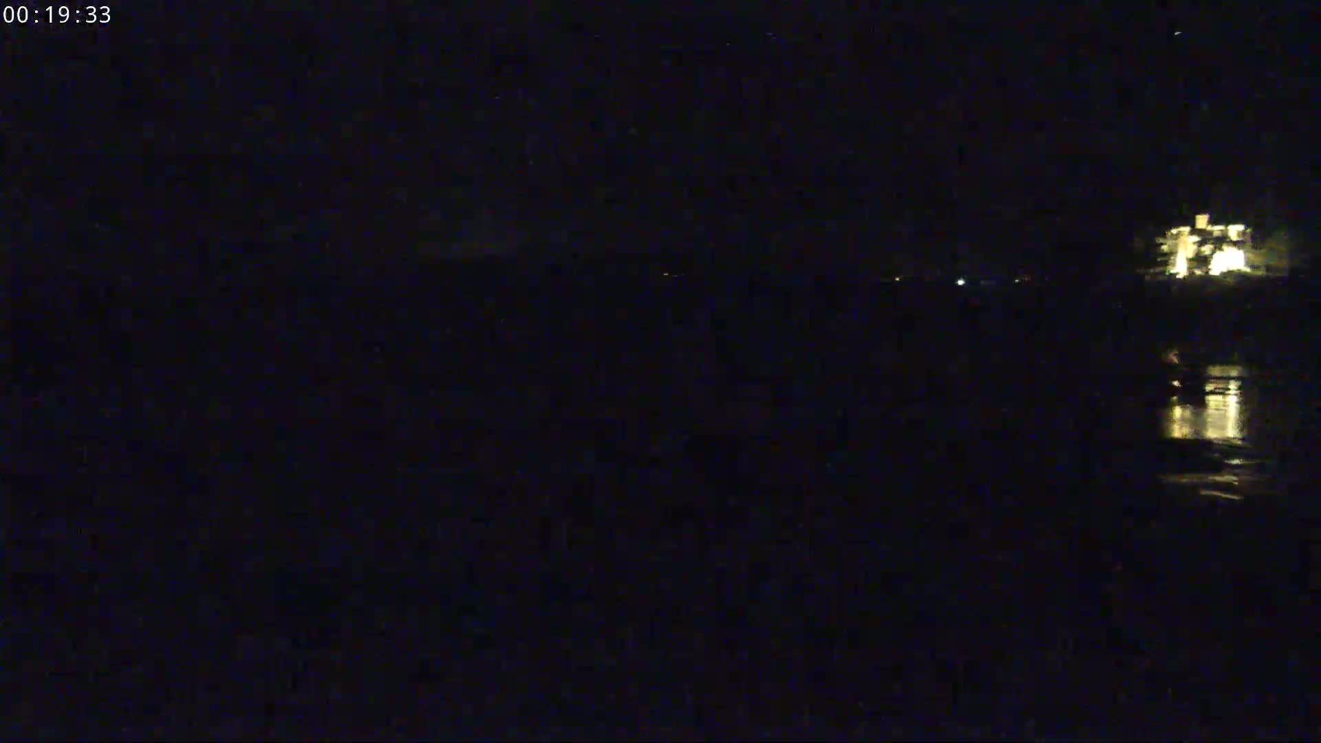 A nighttime, low-light view of a body of water reflecting some lights from a structure in the distance.