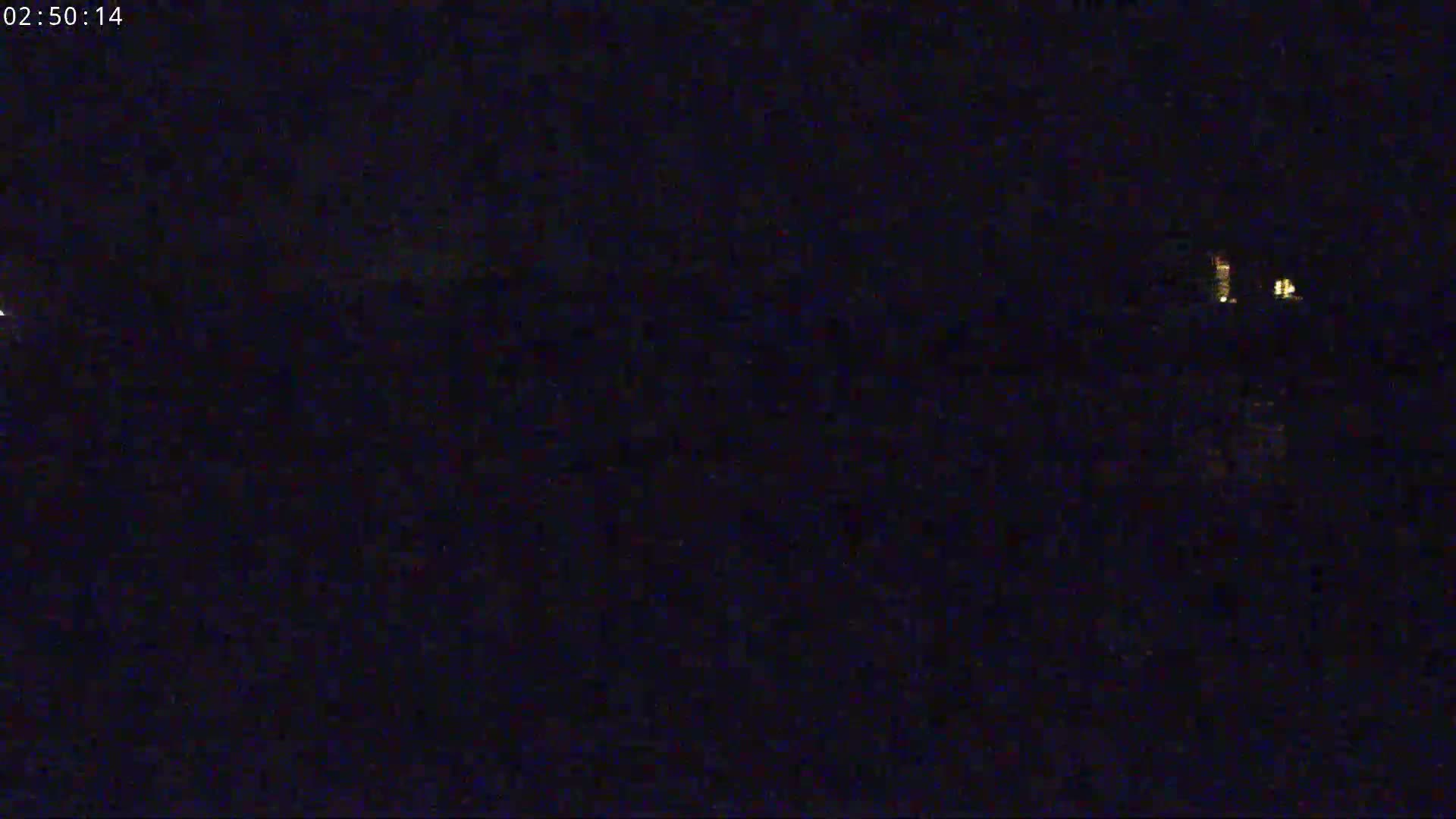 A nighttime, dark scene shows a few distant lights faintly visible in the distance.
