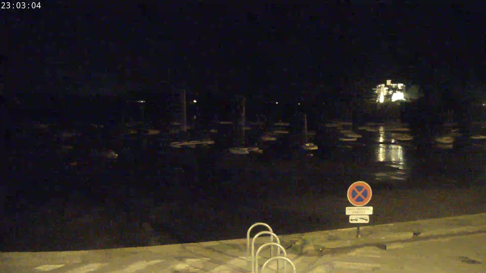 A nighttime view of a calm body of water with boats docked, a no-parking sign, and bike racks in the foreground.