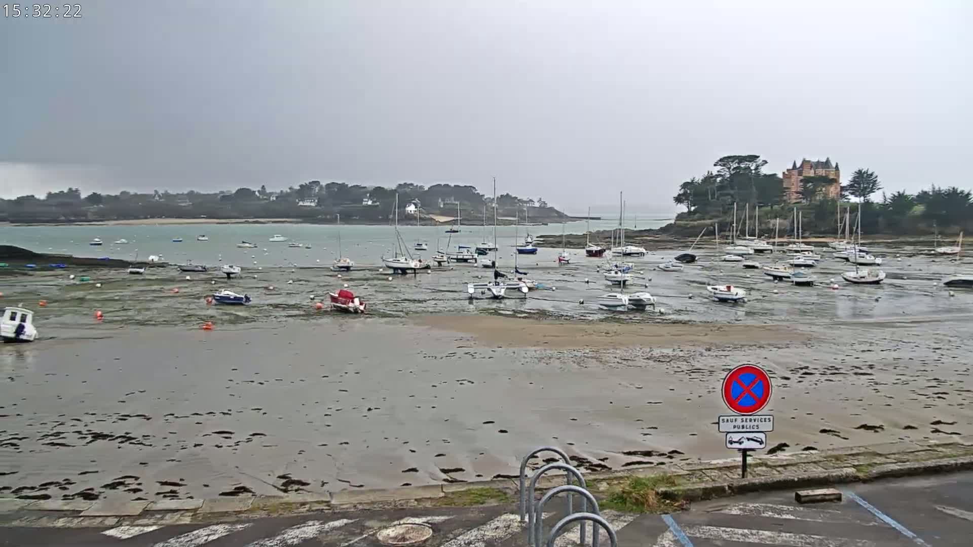 Many sailboats are docked in a harbor at low tide under an overcast sky.
