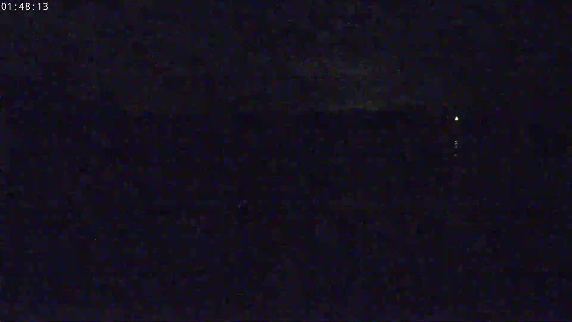 A dark, nighttime scene shows a body of water with a few faint lights visible in the distance.