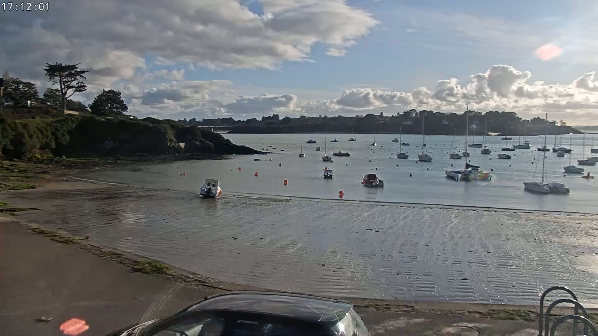 A calm bay with numerous boats at anchor is visible under a partly cloudy sky.