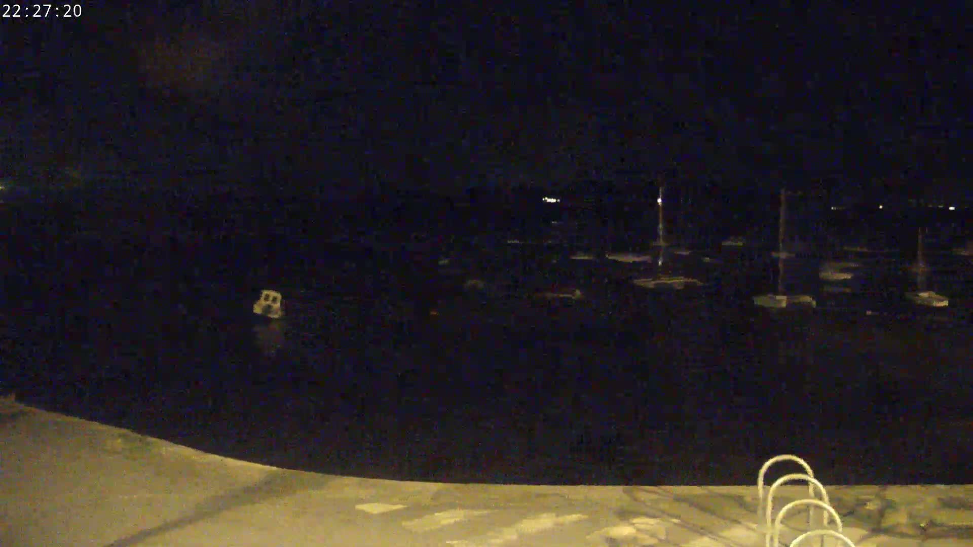 A nighttime view of a dark body of water with several boats docked, and a set of ladder-like steps leading down to the water's edge.