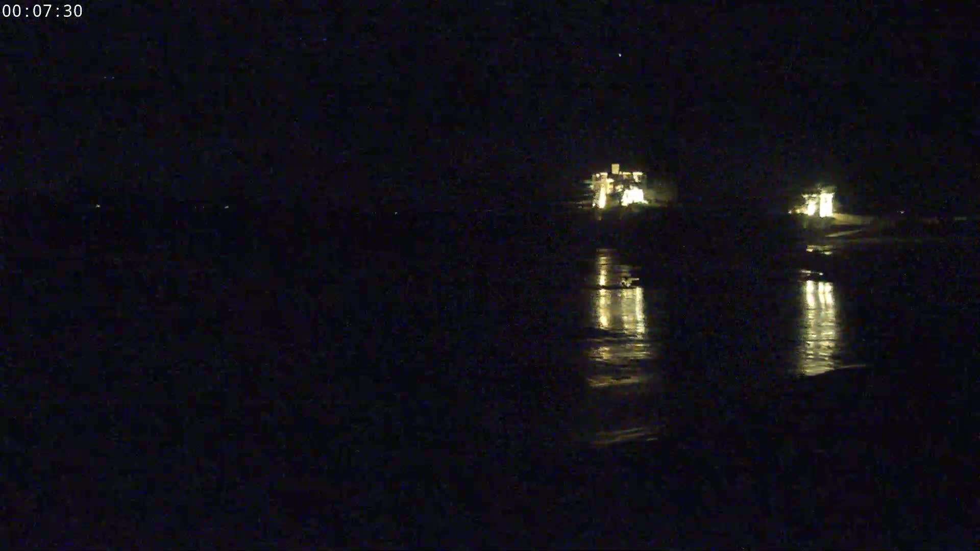 At night, the lights of buildings near a body of water are reflected on the dark surface.