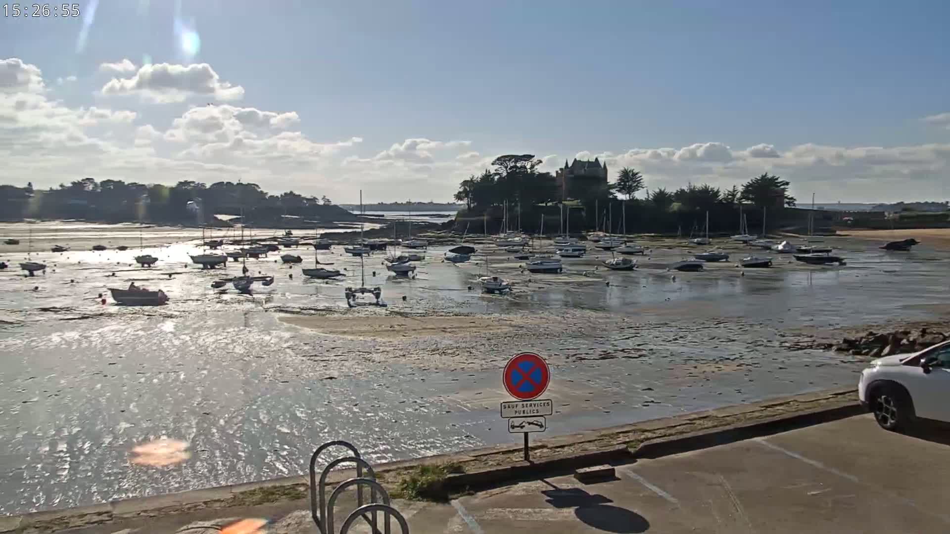 Many sailboats are docked in a harbor at low tide under a partly cloudy sky.