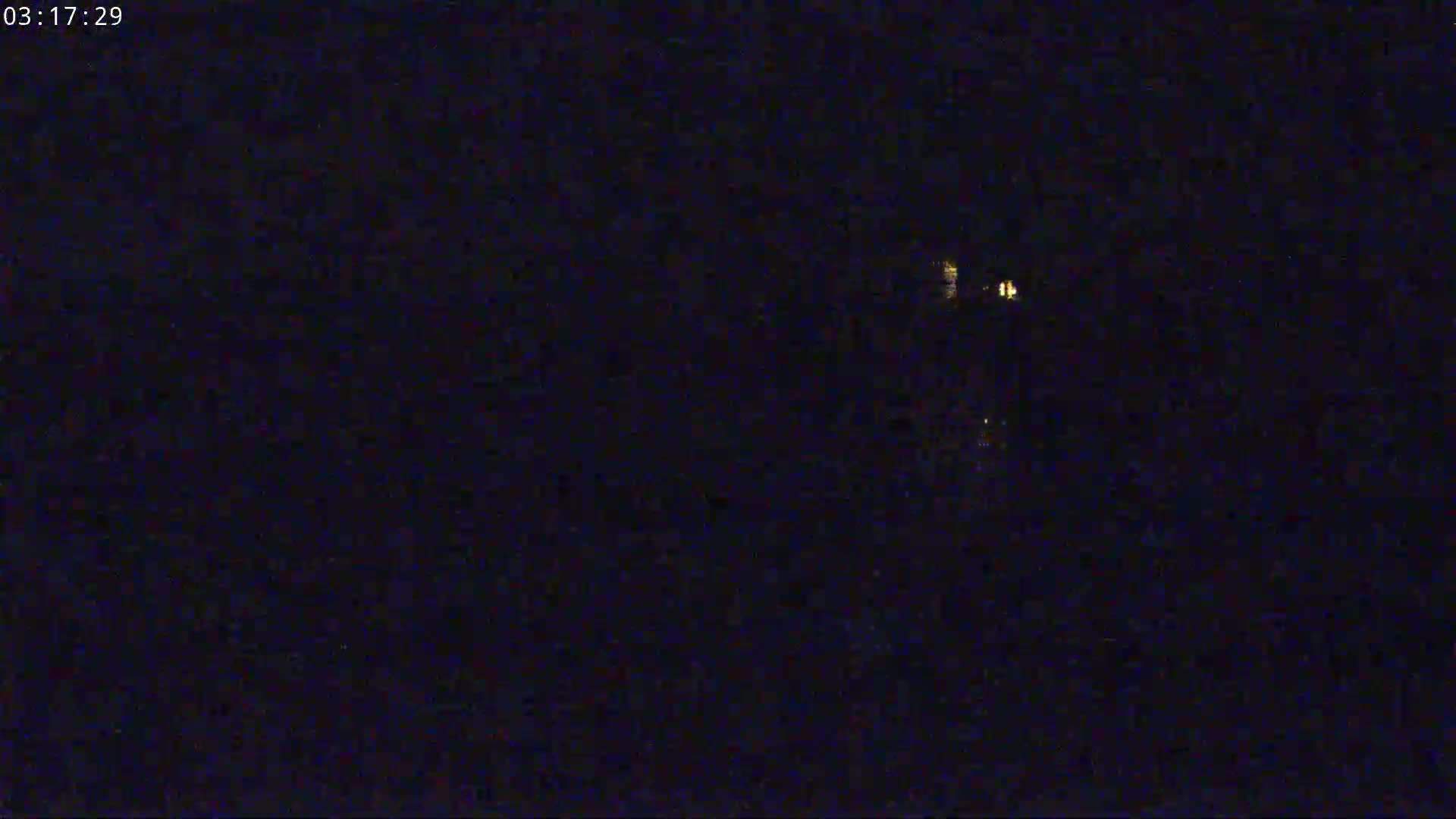 A very dark, nighttime image shows a few small, faint lights in the distance.
