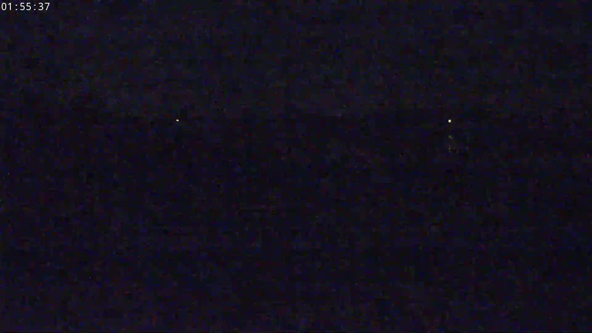 A dark, nighttime scene shows a few faint lights in the distance.
