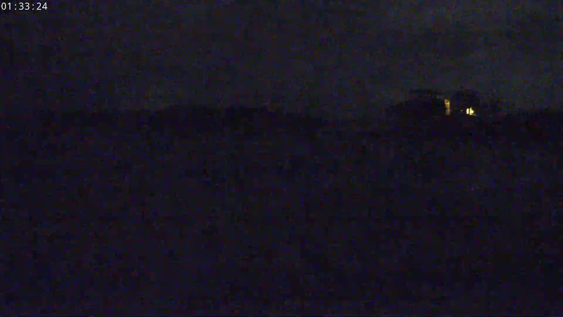 A dimly lit, nighttime scene shows a dark landscape with a few faint lights in the distance.