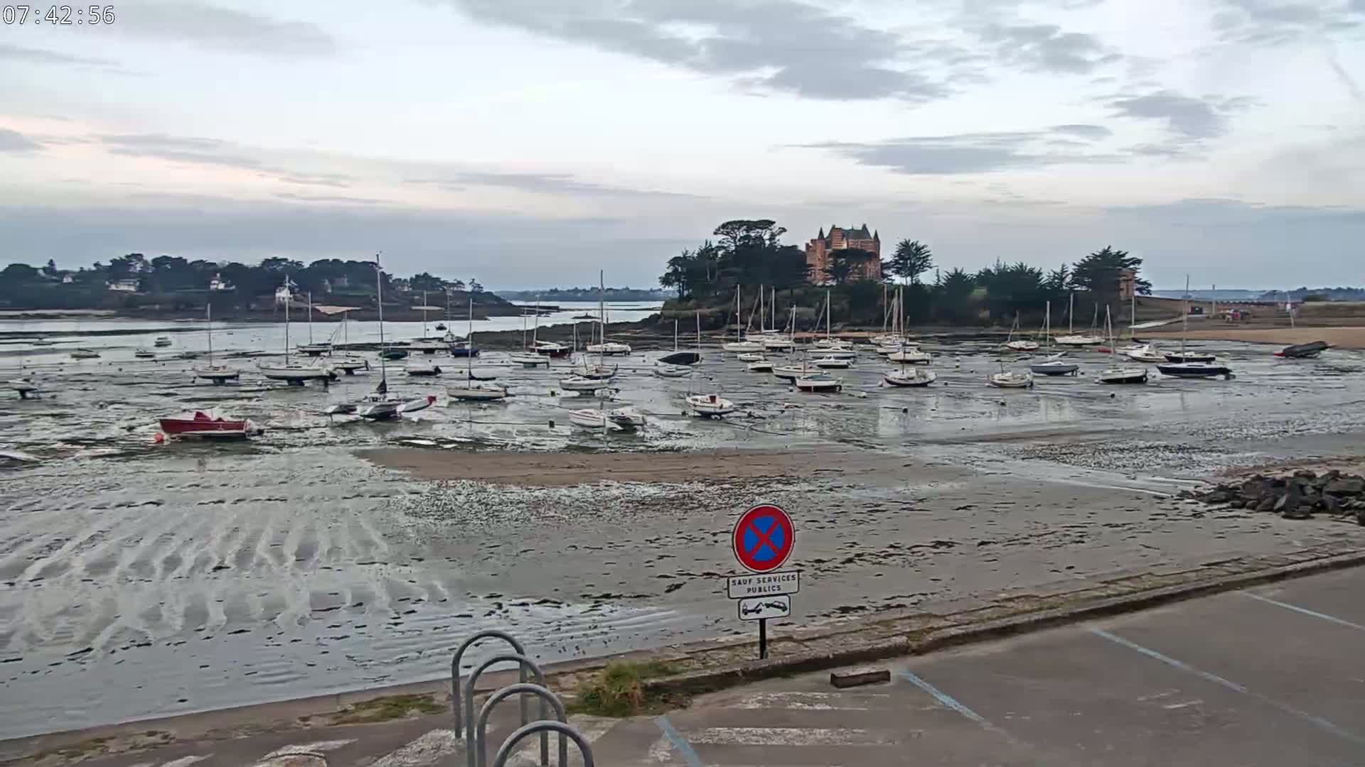 Many sailboats are grounded in a harbor at low tide under an overcast sky.