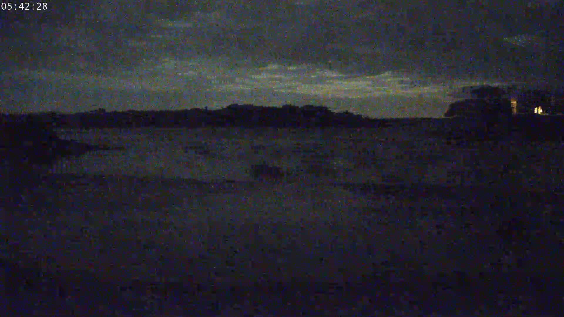 A dark, nighttime scene shows a flat expanse of land under a mostly cloudy sky.