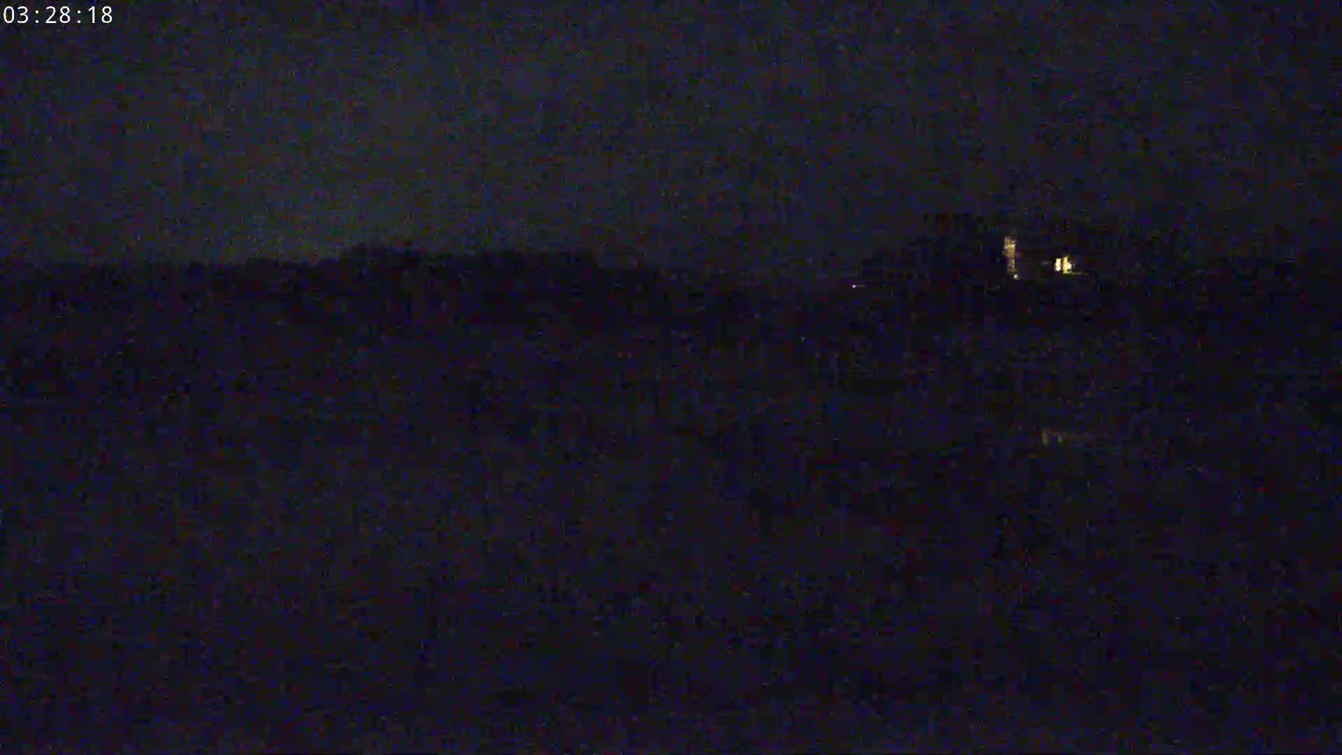 A dark, nighttime scene shows a dimly lit building in the distance, under a mostly clear sky.
