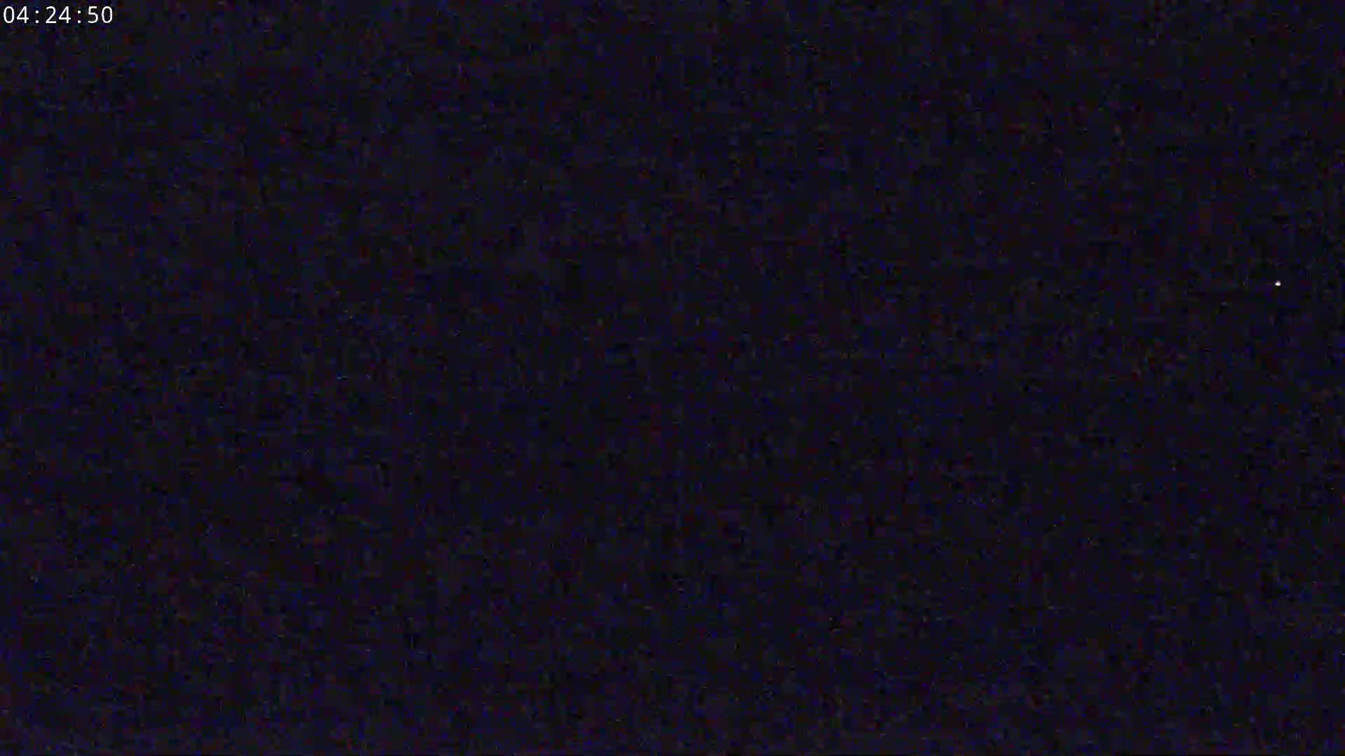 The image shows a dark, grainy nighttime scene with a single, faint light visible in the upper right corner.