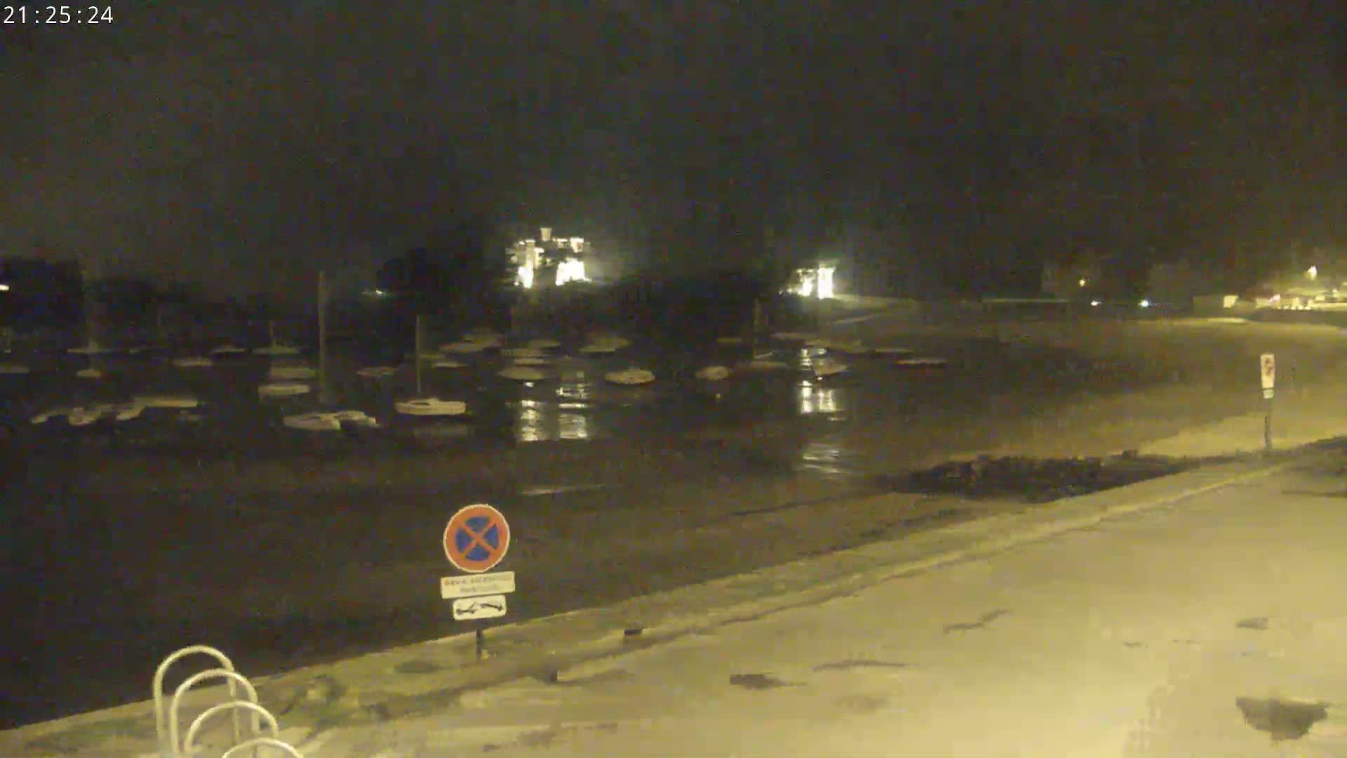 At night, numerous boats are moored in a wet, dark marina under a clear sky.