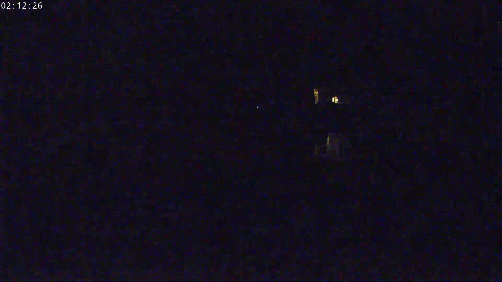 A nighttime, dark image shows a few distant, faint lights possibly from buildings.
