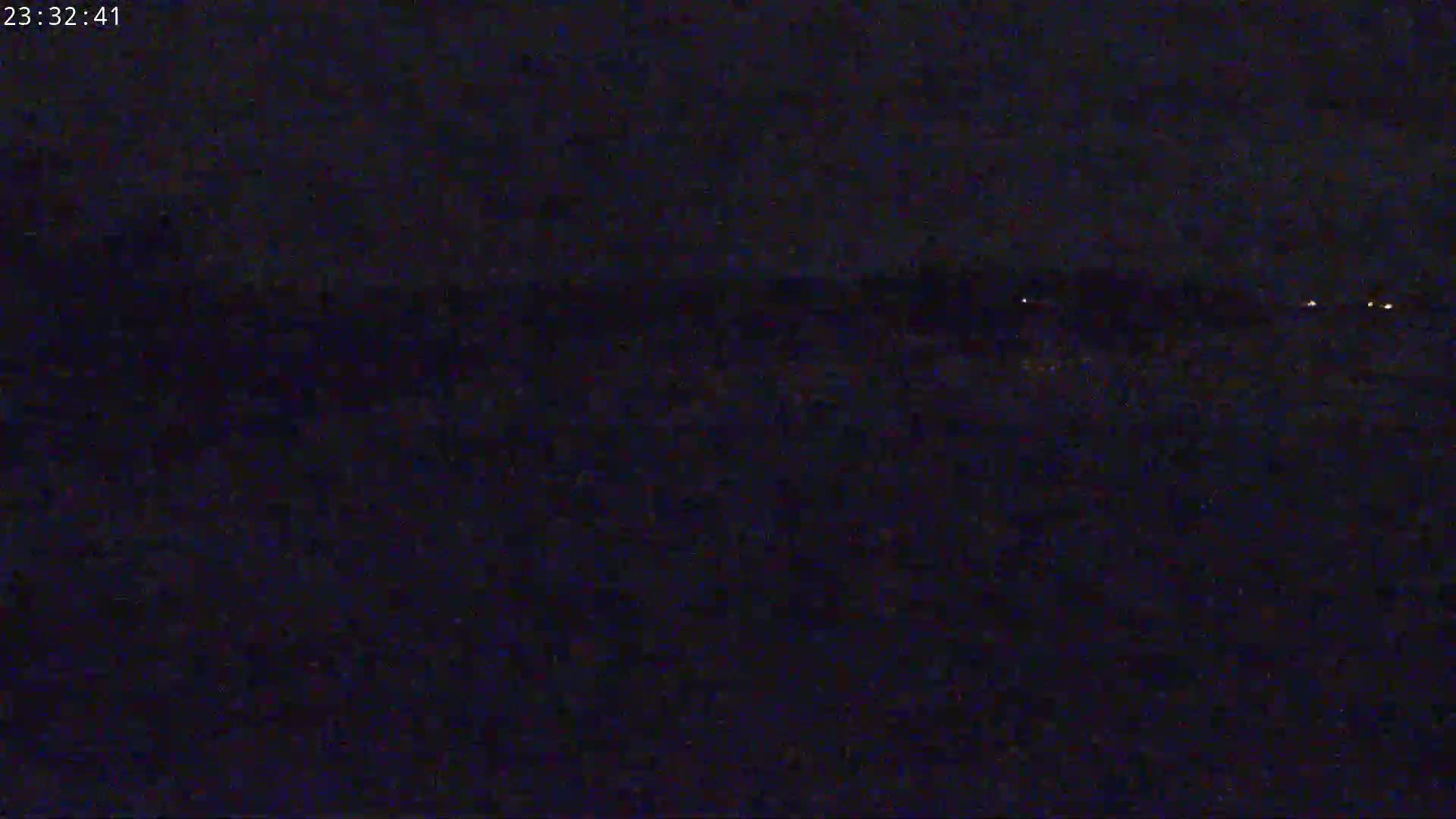 A dark, nighttime scene shows a distant line of faint lights across a dark expanse.