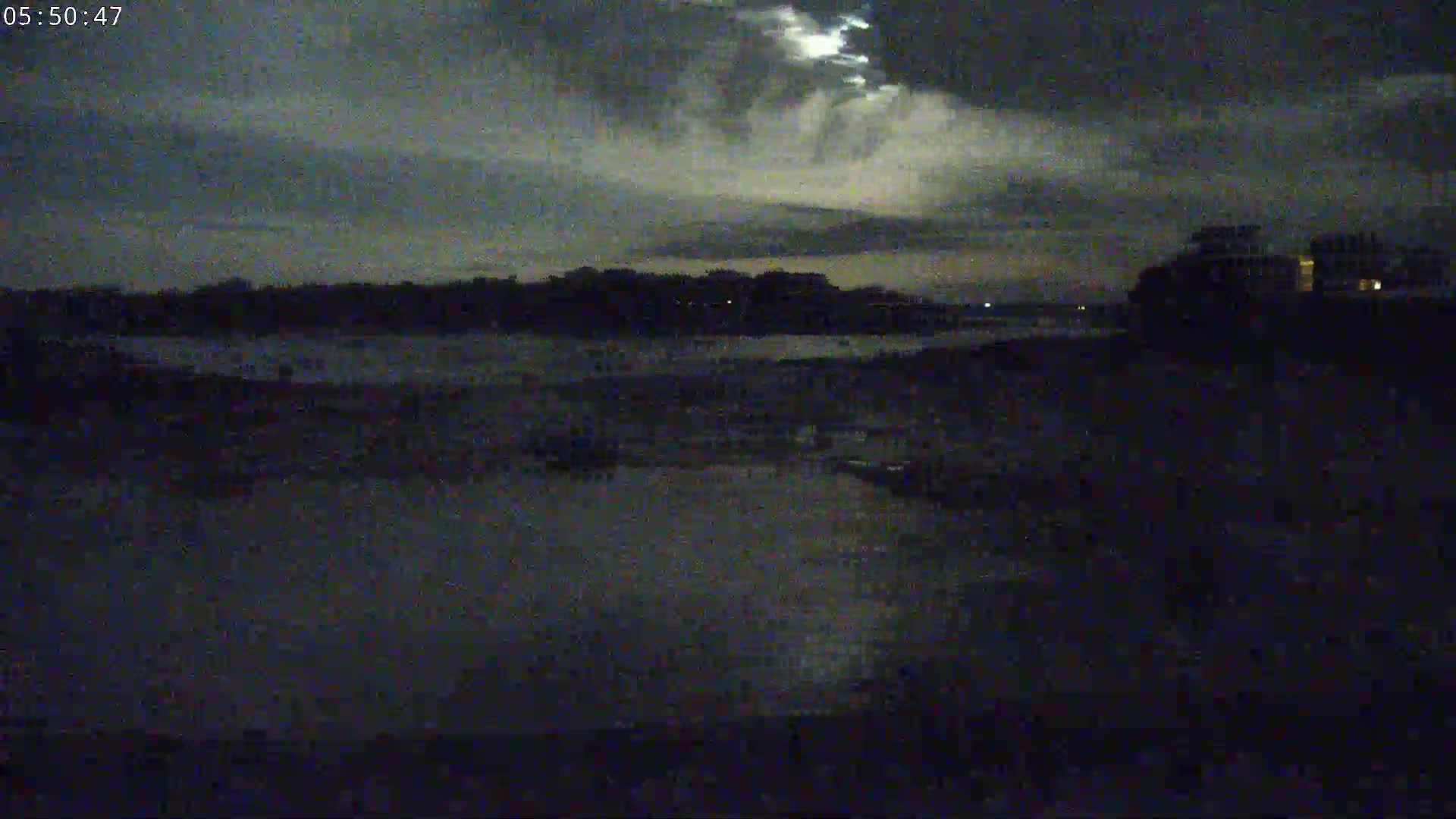 A dark, nighttime scene shows a body of water under a cloudy sky with a hint of moonlight.