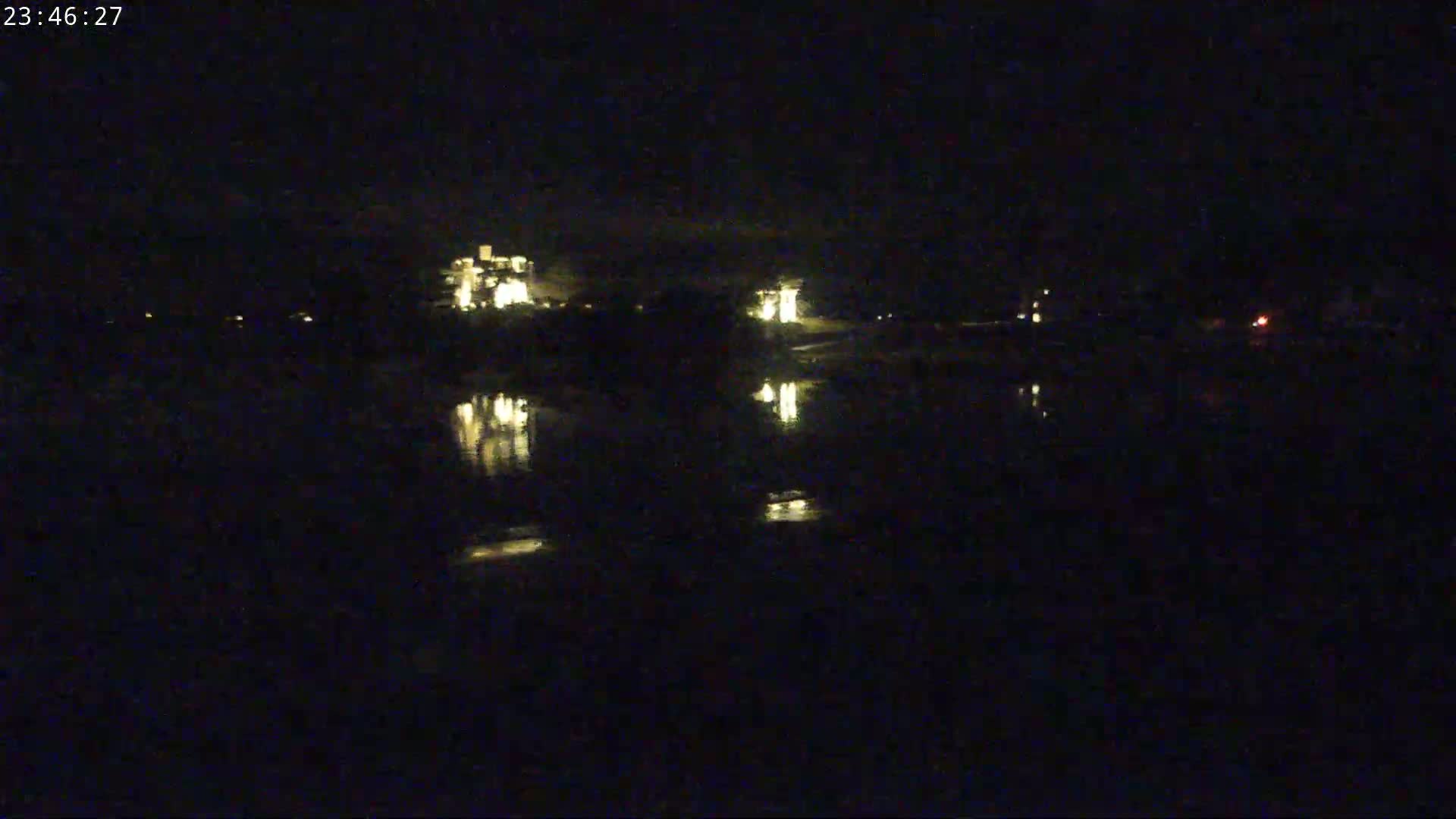 A nighttime view of illuminated buildings reflected in calm water under a dark sky.