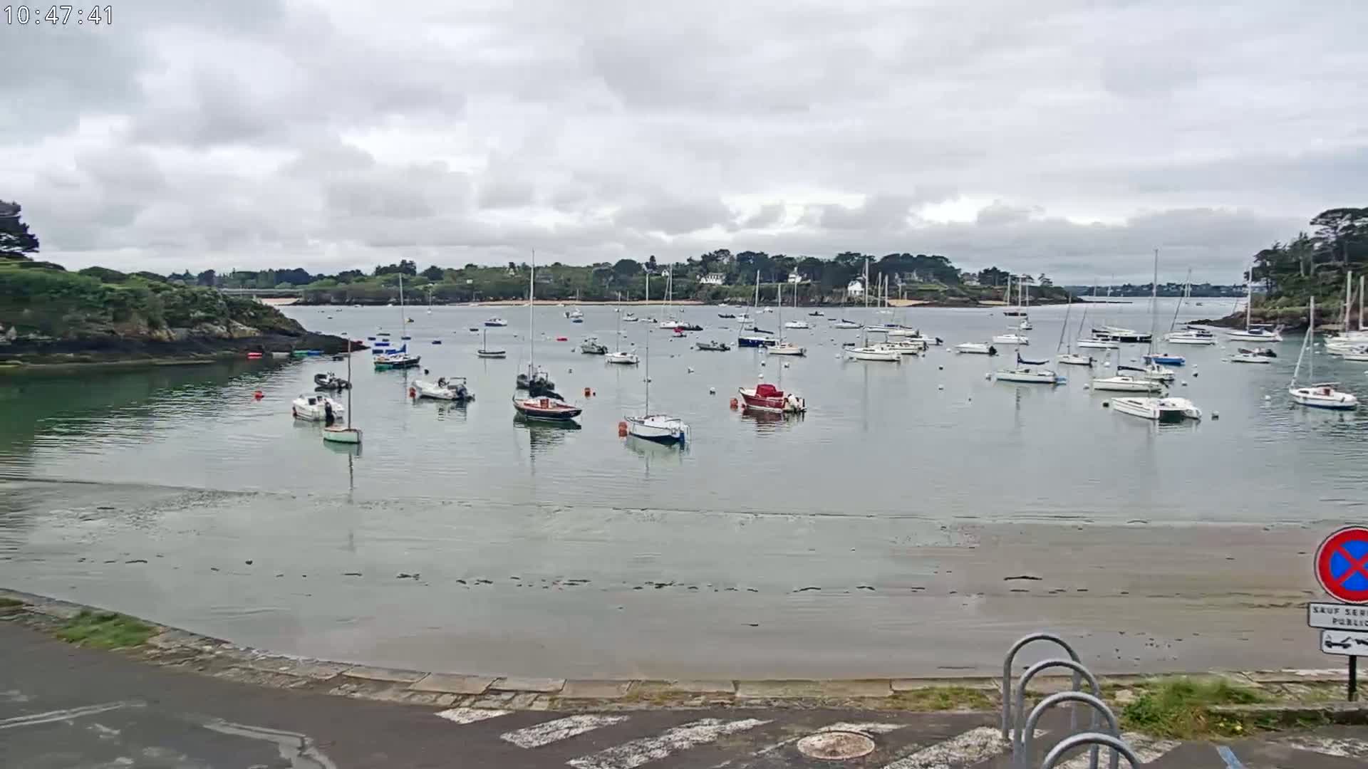 Numerous sailboats are moored in a calm bay under a cloudy sky.