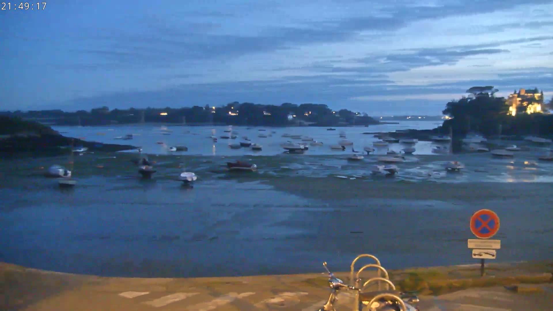 Many small boats are at rest in a calm, twilight harbor, with a landmass visible in the background.