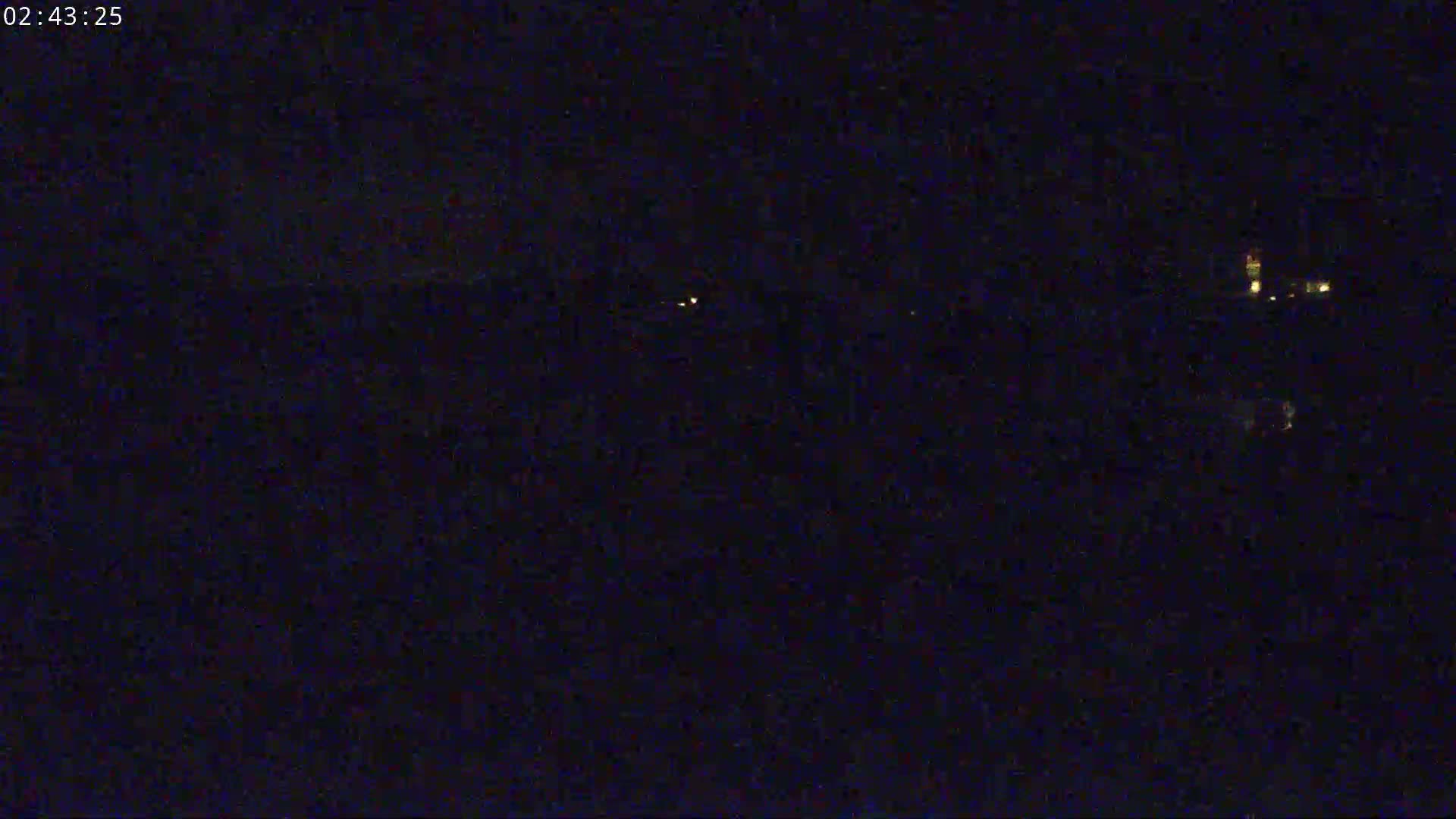 A nighttime, dark image shows a few faint lights in the distance.