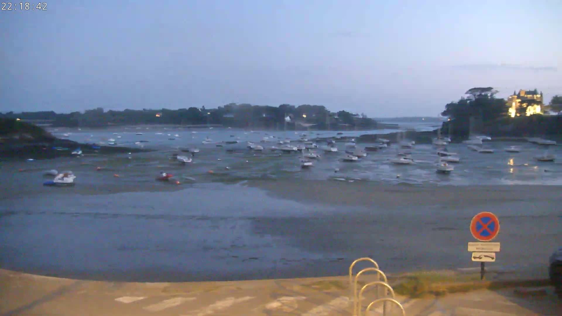 Many small boats are moored in a calm, shallow harbor at twilight.