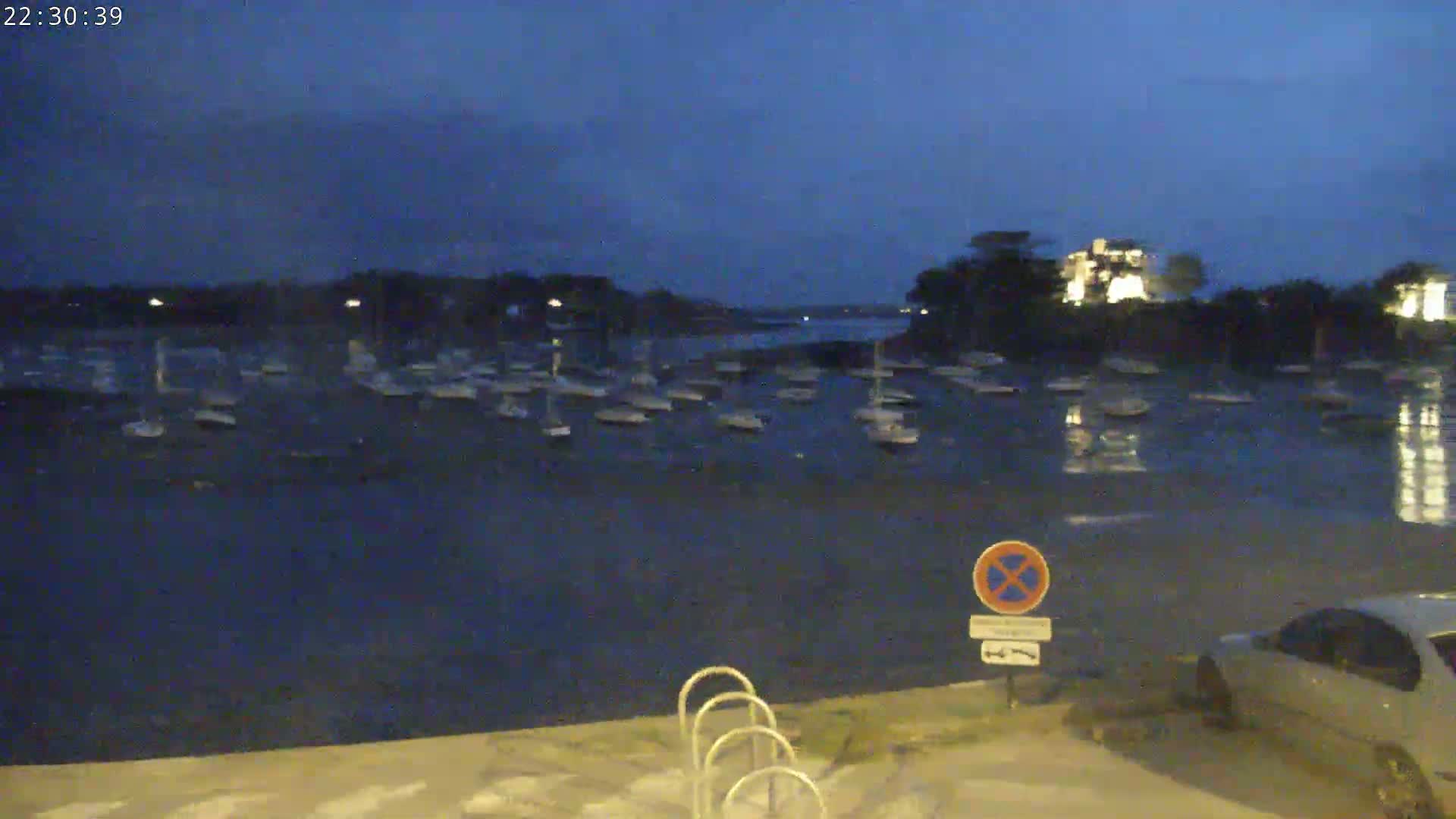 Many sailboats are moored in a calm, dark-blue body of water at twilight.