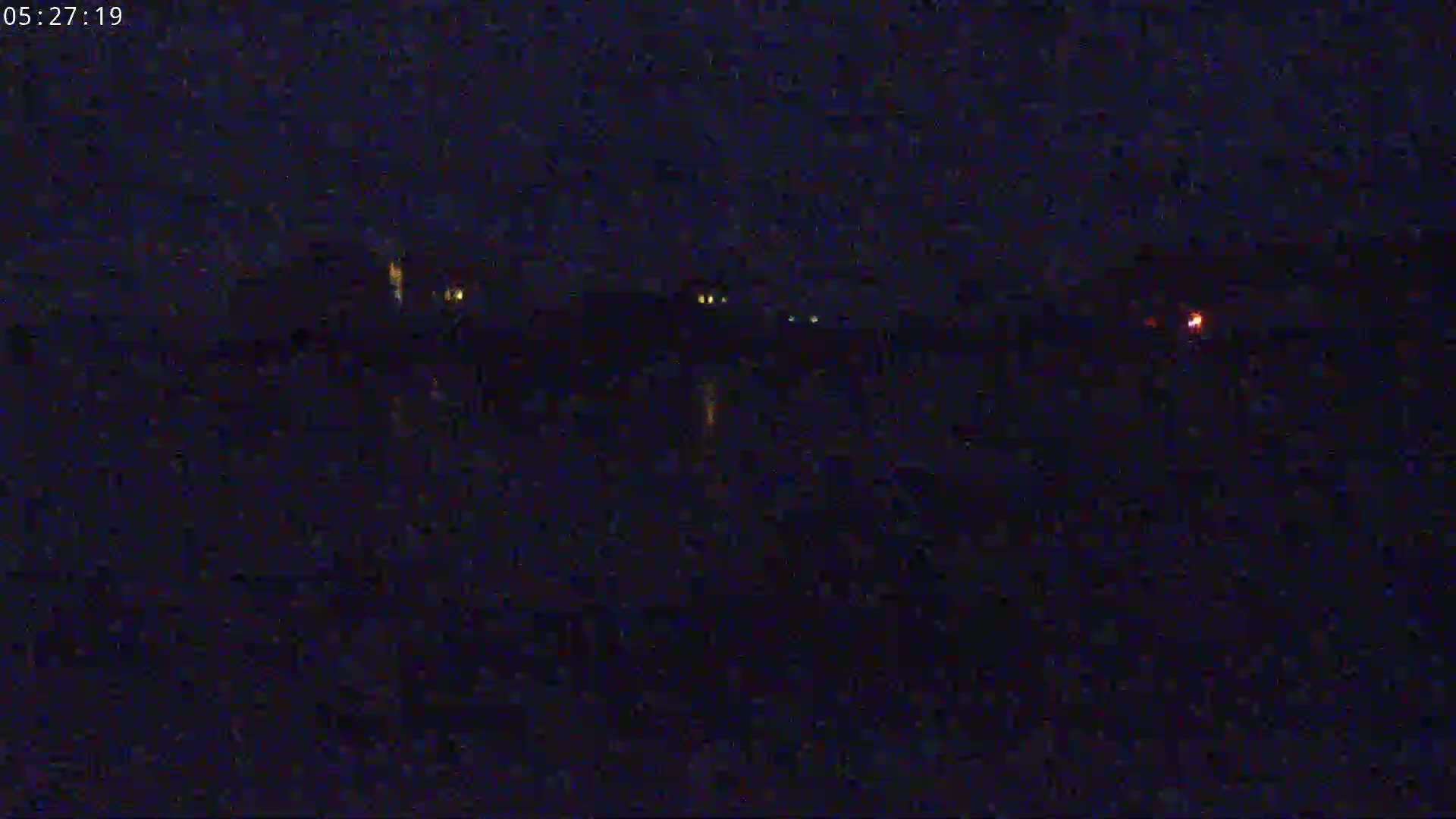 A dark, nighttime scene shows a body of water reflecting faint lights from buildings across the shore.