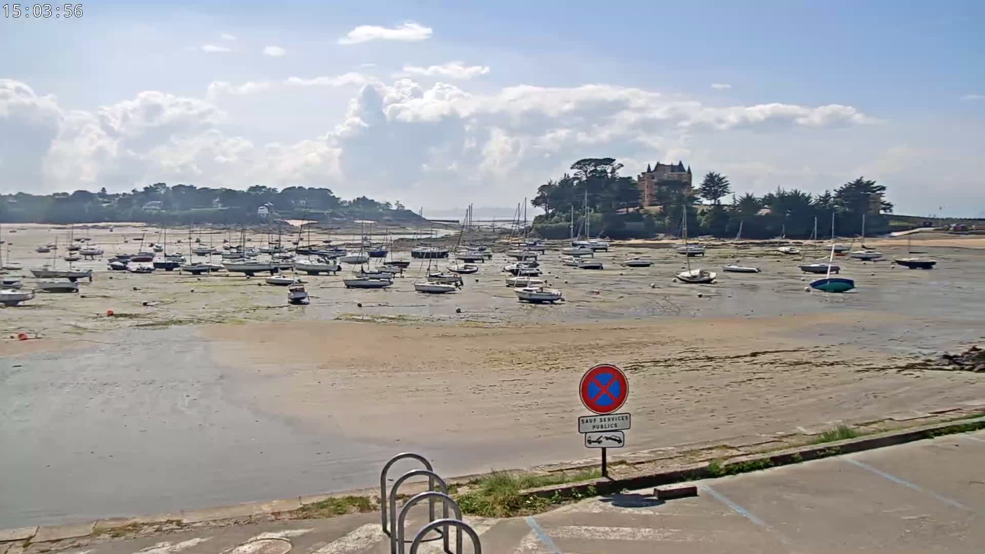 Many sailboats are grounded on a sandy, low-tide beach under a partly cloudy sky.