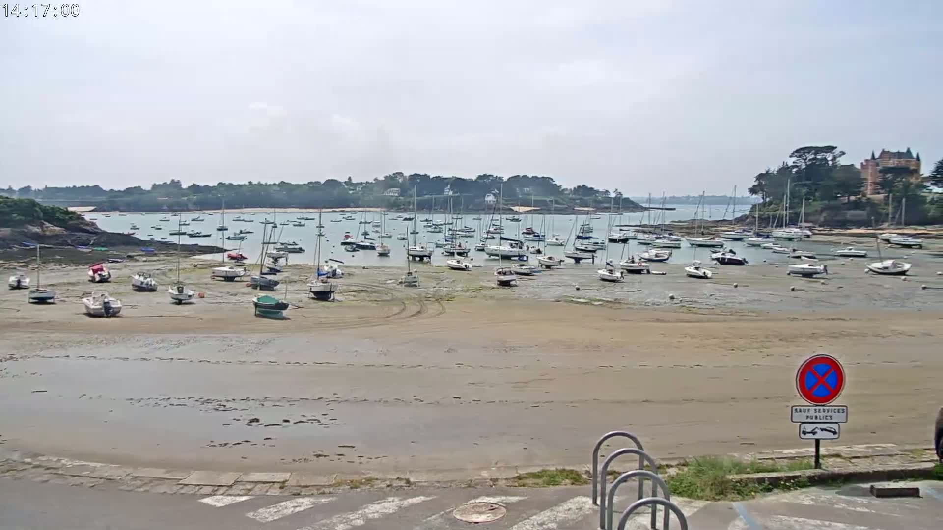 Numerous sailboats are beached on a sandy shore during a partly cloudy day.