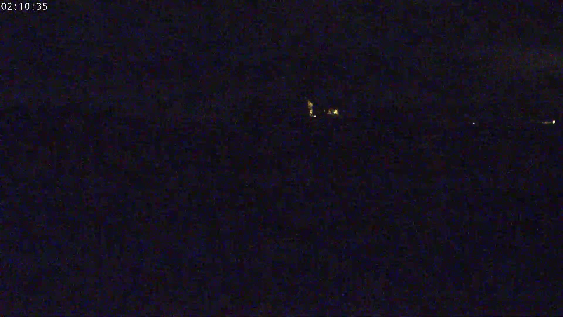 A nighttime, dark image shows a few distant lights on the horizon.