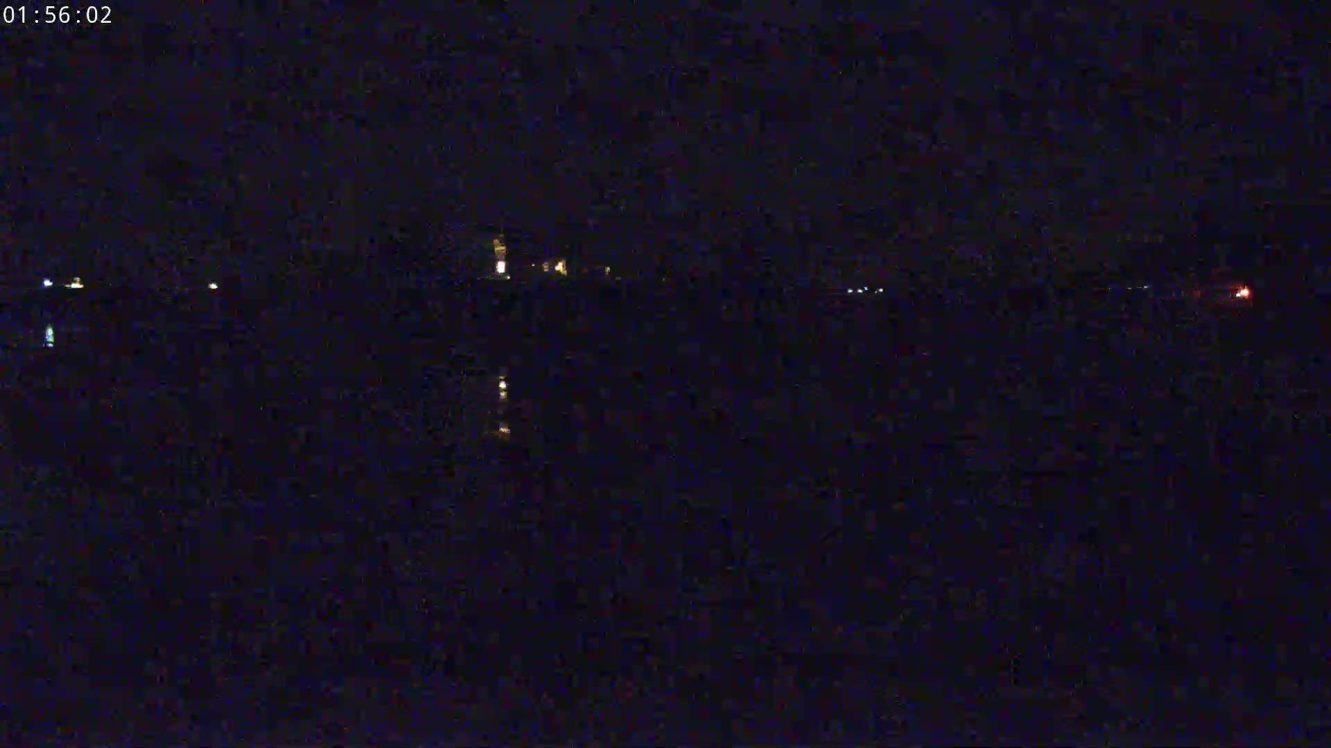A dark, nighttime view of a body of water reflecting a few distant lights.