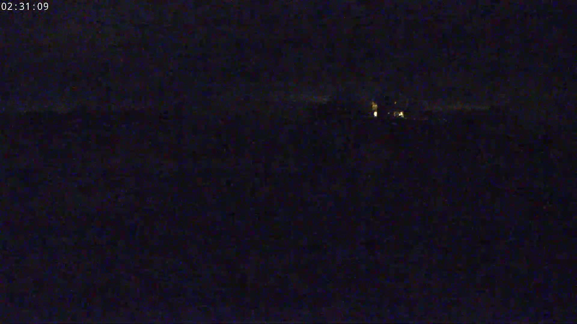 A dark, nighttime scene shows a few faint lights in the distance.