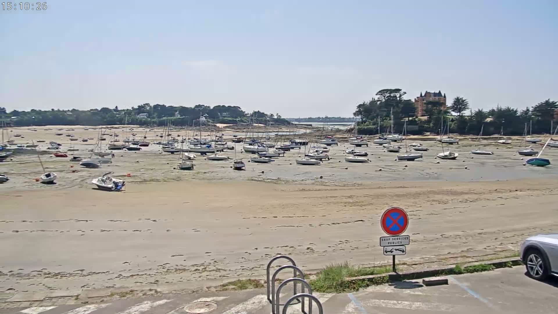 Many sailboats are grounded on a wide, sandy beach at low tide under a clear, sunny sky.