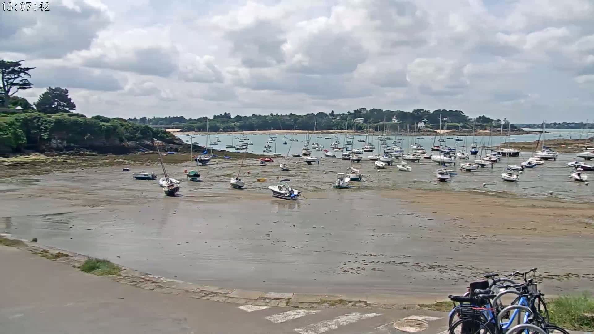 Many sailboats are grounded on a wide, exposed sandbar in a calm bay under a partly cloudy sky.
