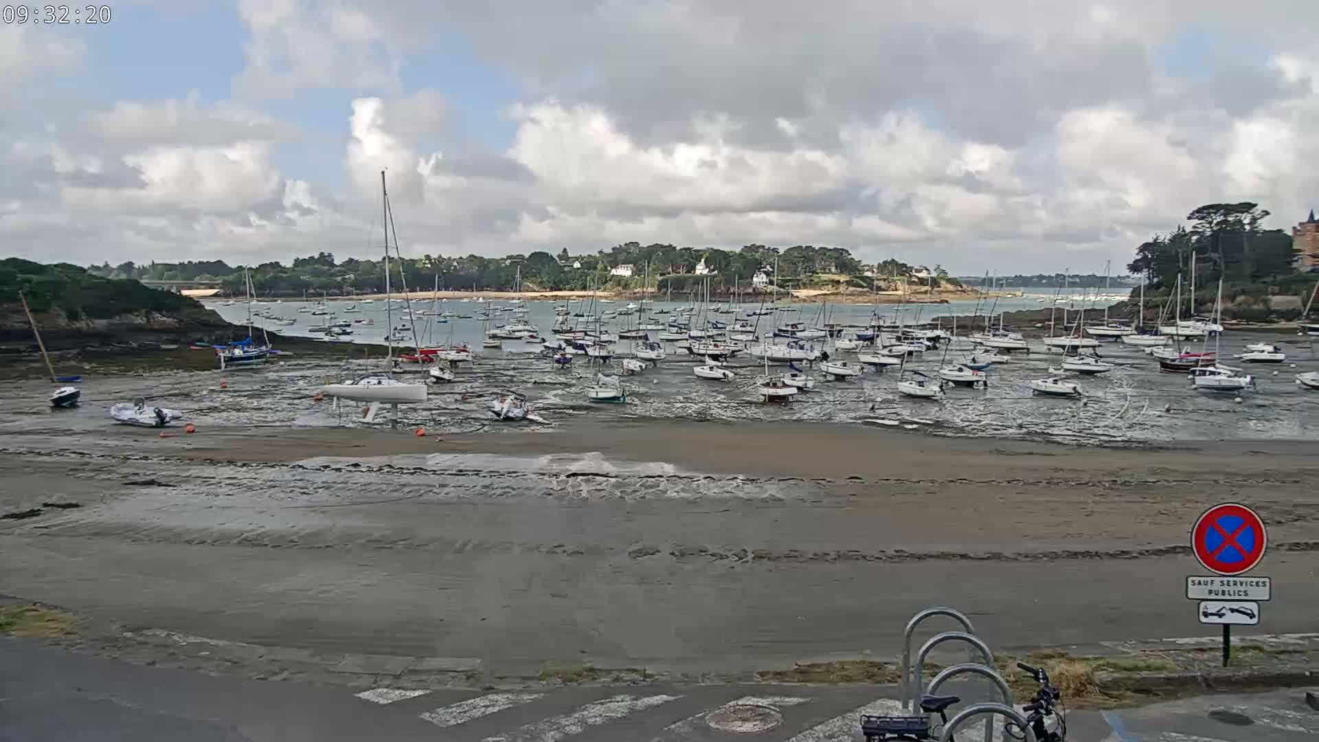 Many sailboats are grounded on a sandy shore at low tide under a partly cloudy sky.
