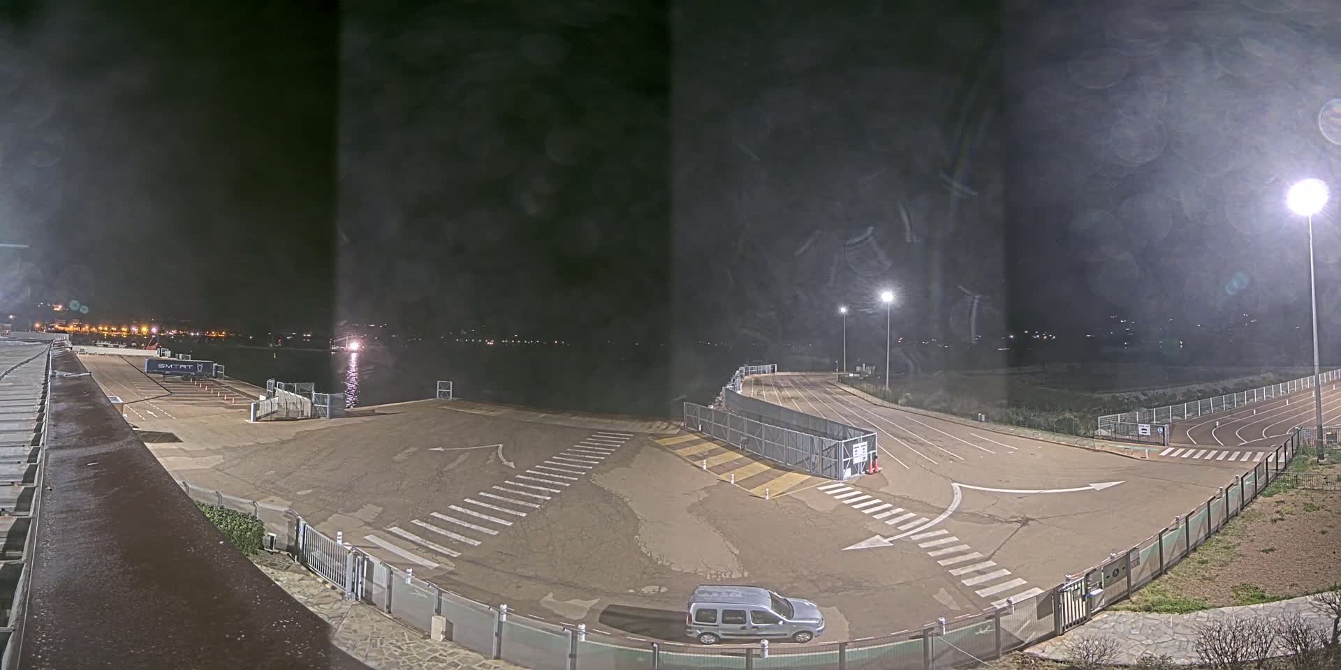A nighttime view of an empty parking lot and roadway near a body of water, illuminated by artificial lights.