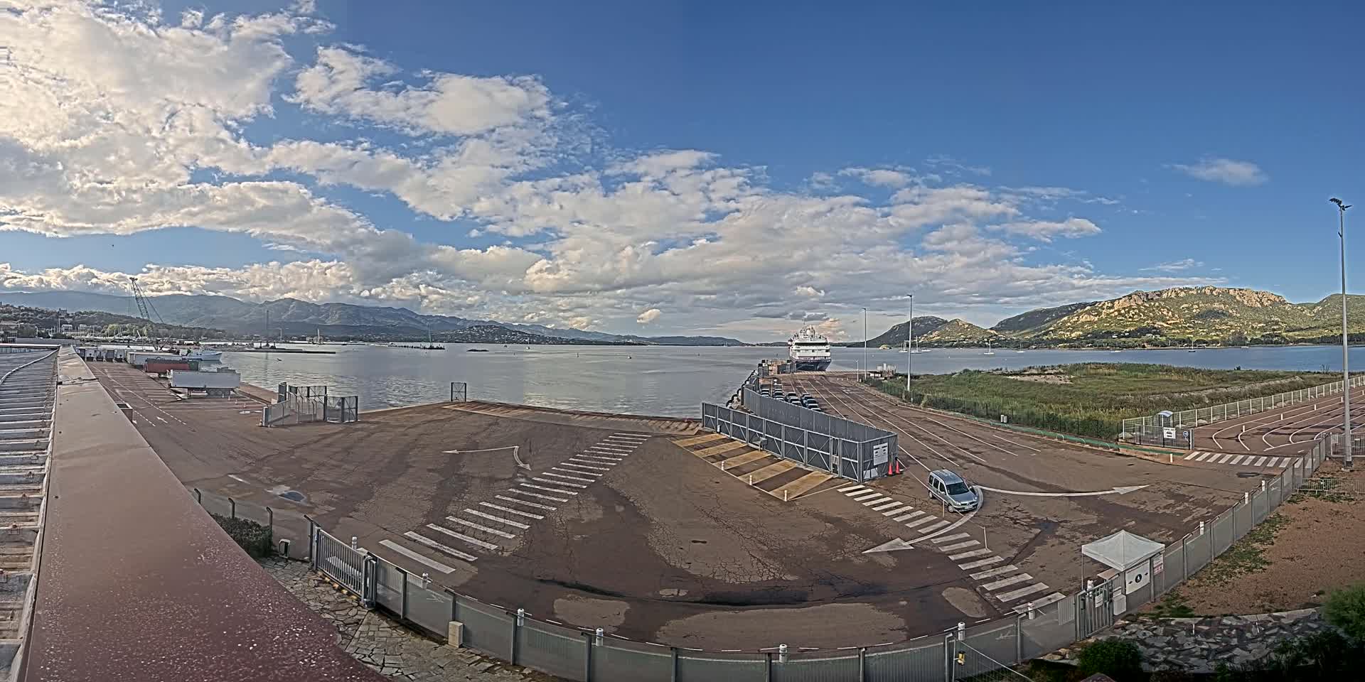 A mostly empty port area with a large ferry docked, under a partly cloudy sky.