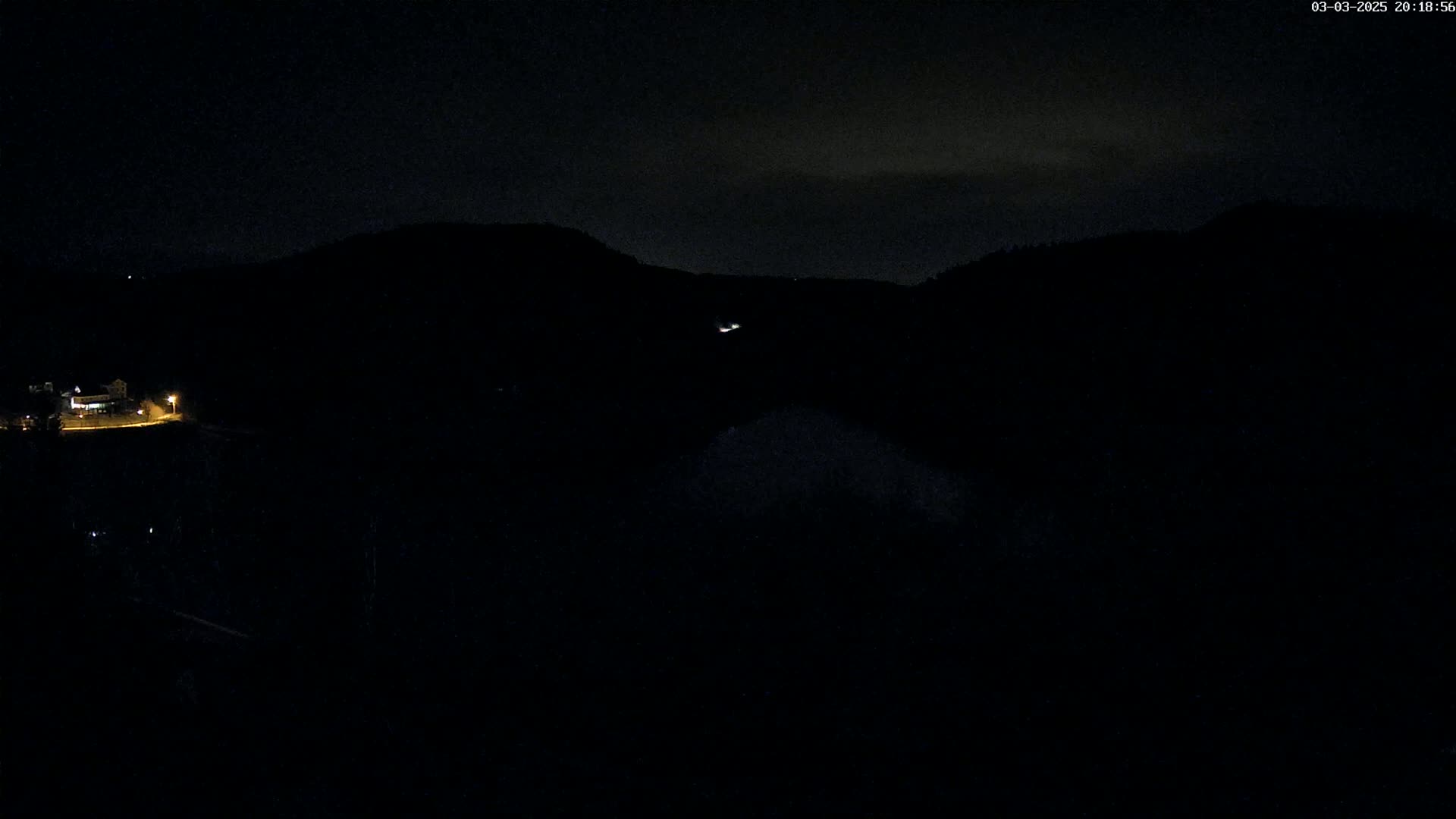 A nighttime view of dimly lit buildings and dark hills under a mostly clear sky.