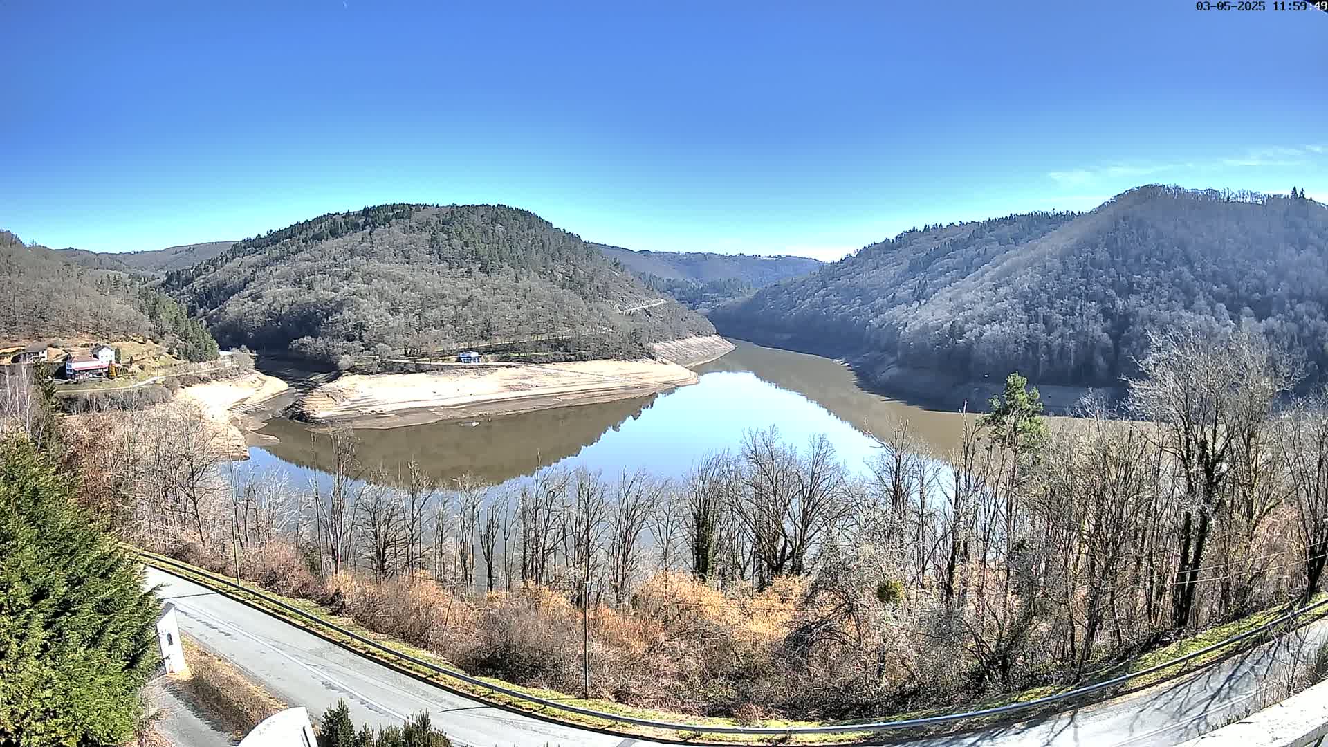 A partly dry reservoir curves between hillsides of bare, winter trees under a clear blue sky.