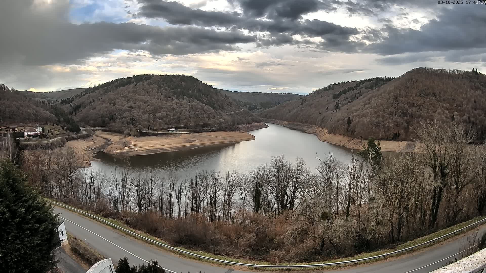 A winding river flows through a valley of bare, brown trees under a cloudy sky.