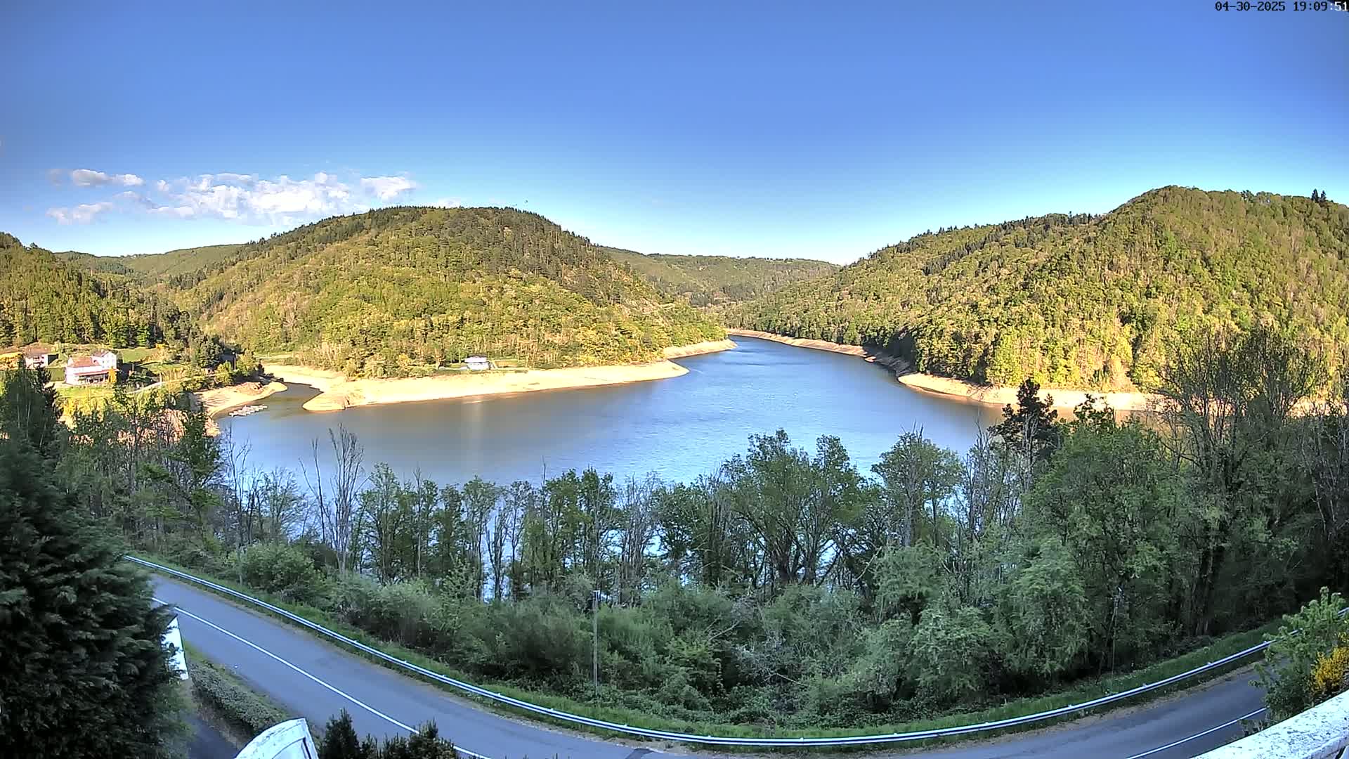 A winding river flows through a valley of lush green hills under a clear blue sky.