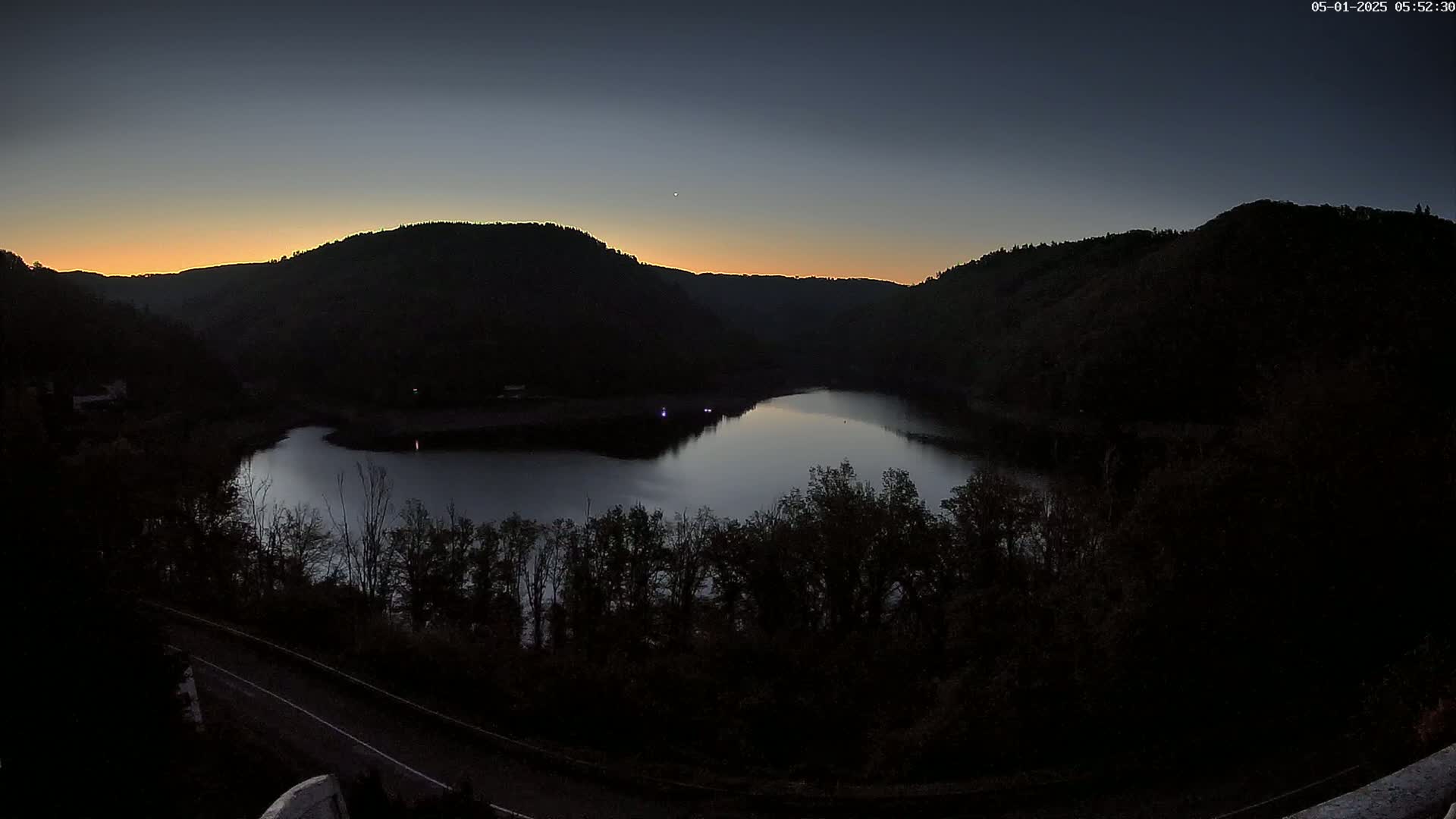 A calm lake nestled between dark, silhouetted hills at sunrise.