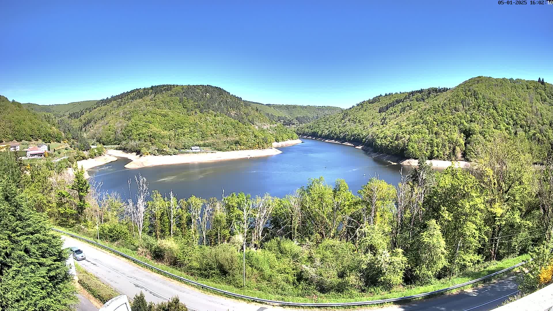 A tranquil lake curves between lush green hills under a clear blue sky.