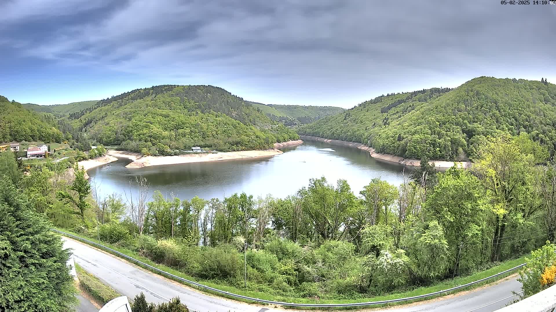 A calm river curves through a valley of lush green hills under a cloudy sky.