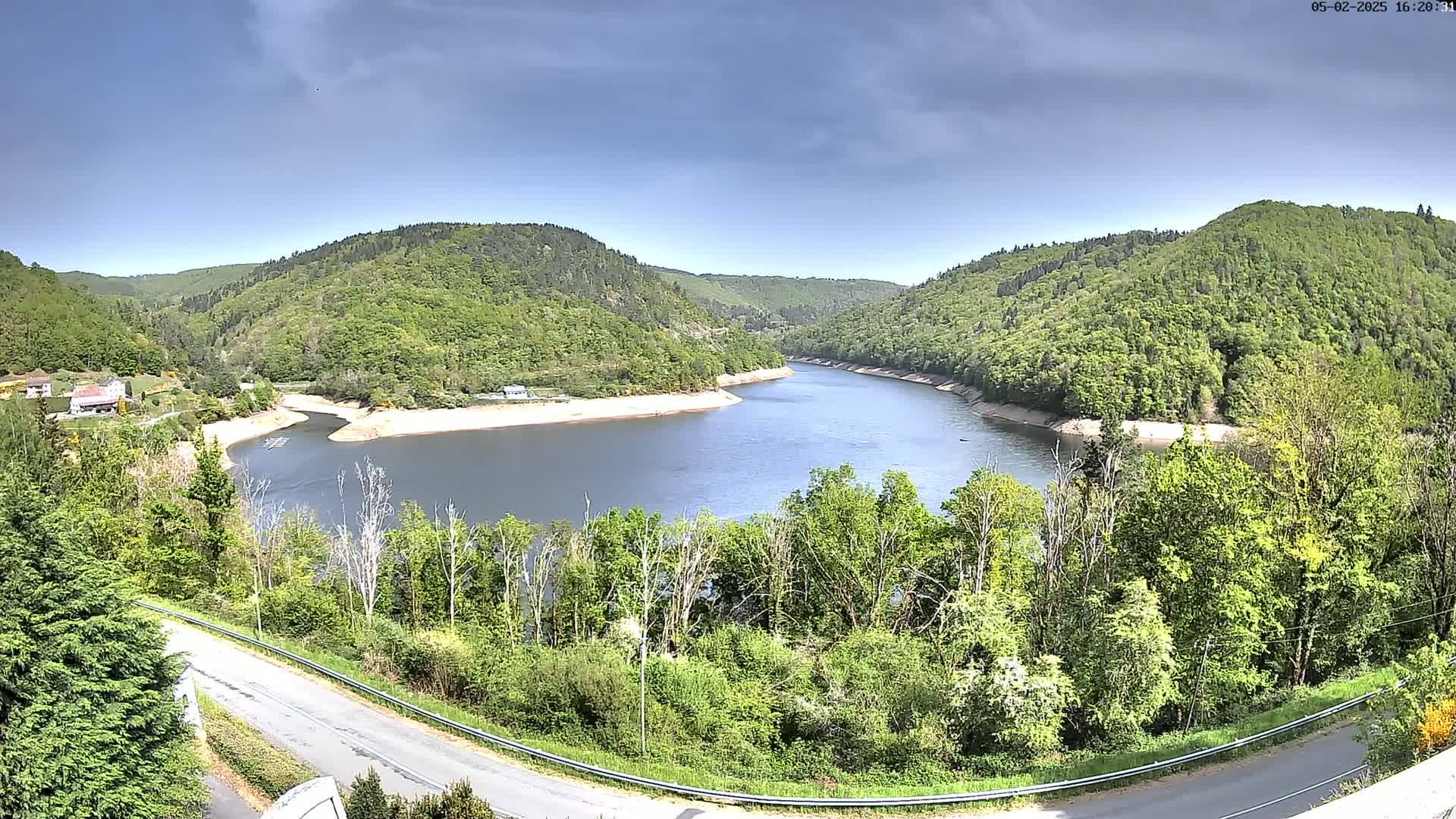 A tranquil river curves through a lush green valley under a partly cloudy sky.