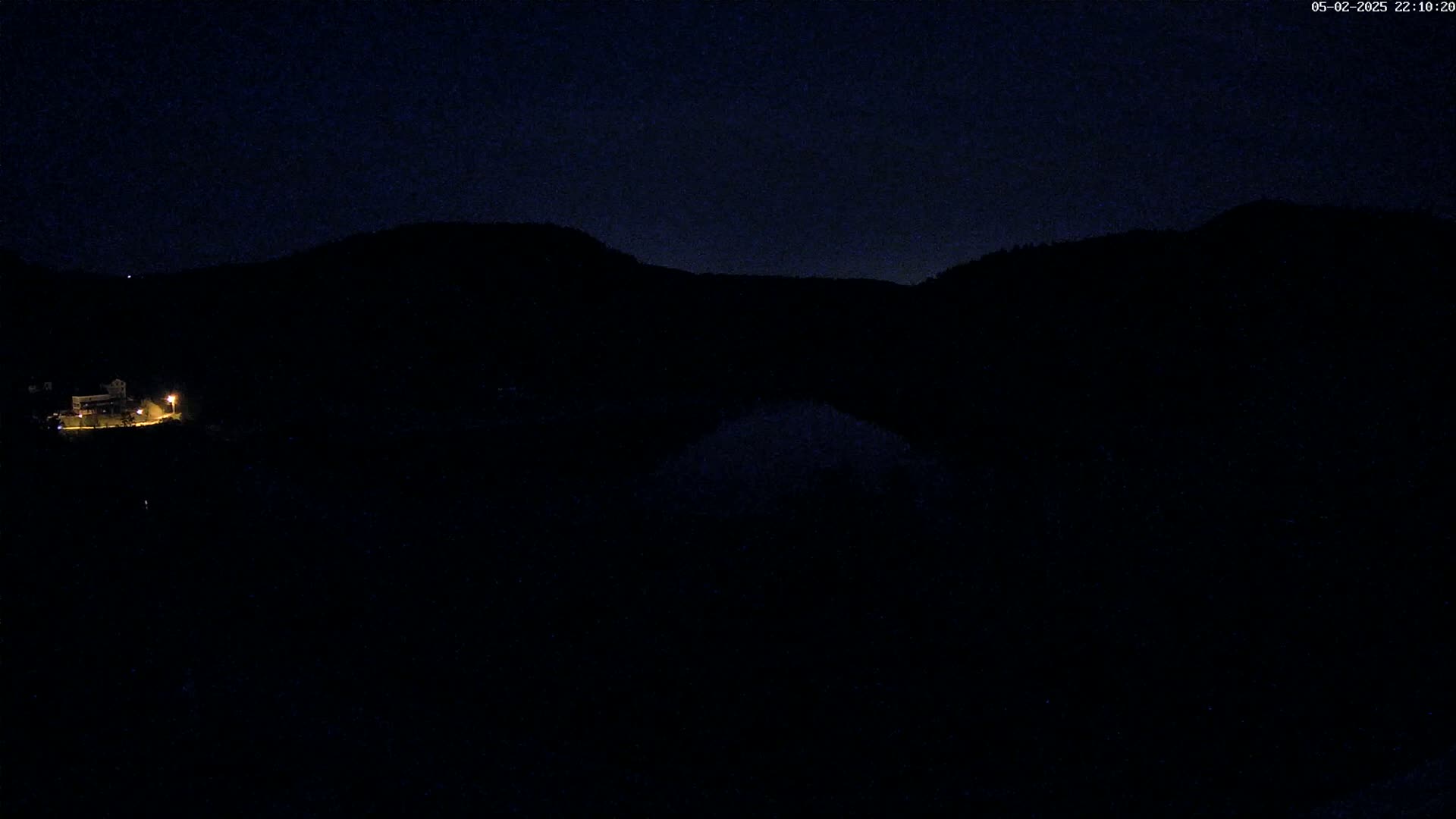 A dimly lit building sits on a dark hillside under a night sky.